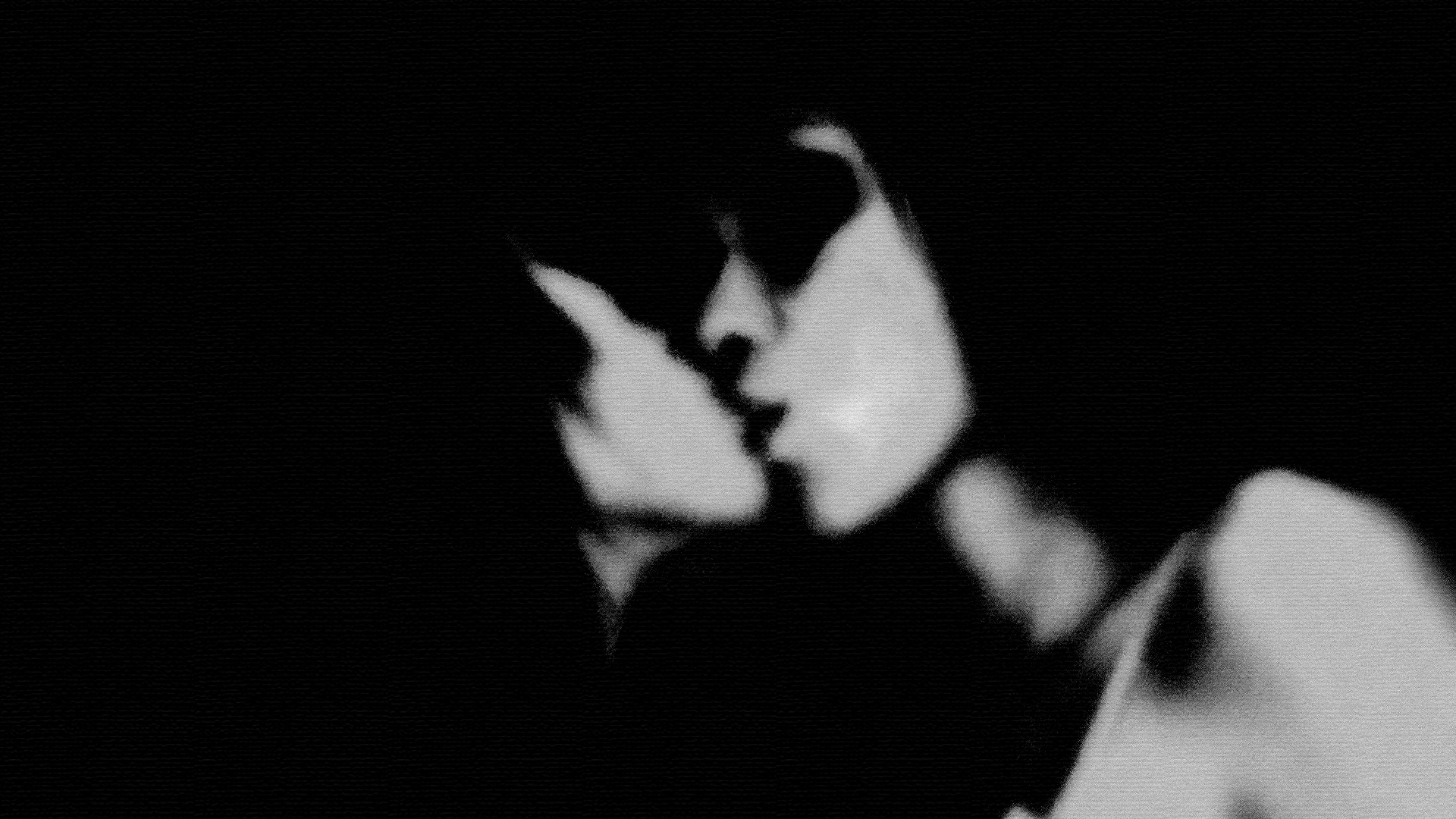Black and white photo of two women with short hair and glasses, kissing each other.