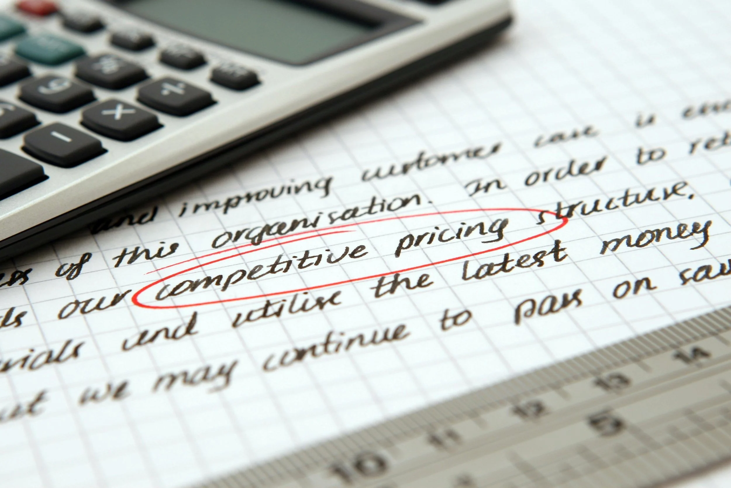 Handwritten notes on graph paper with a calculator resting on top, with the words 'competitive pricing' underlined in red.