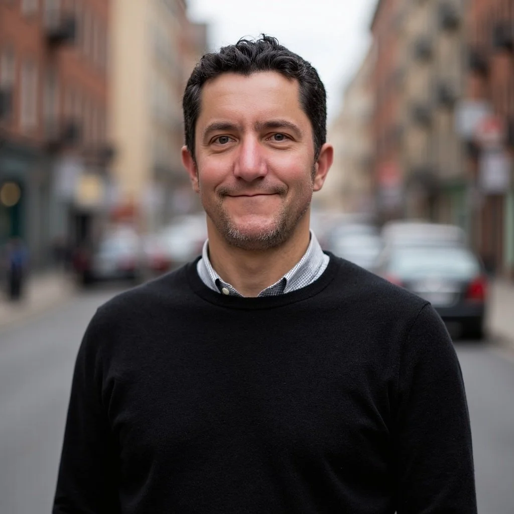 A photo of Geoff Mosher, the founder of Mosher Enterprises: he has dark hair and is smiling while standing on a city street with blurred buildings and parked cars in the background.
