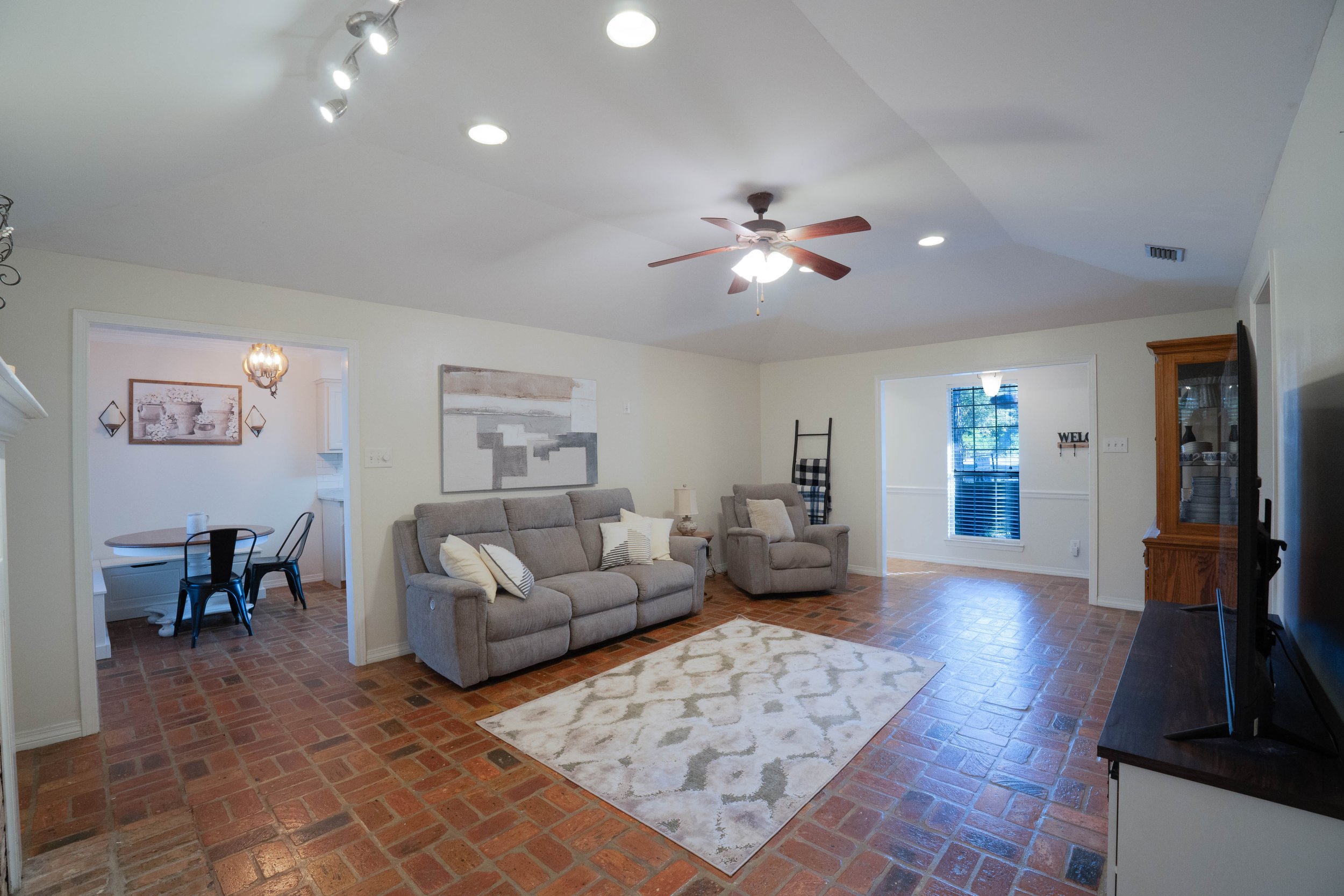 Living room with brick flooring, grey sofa, armchair, area rug, ceiling fan, and wall art. Mobile, Alabama