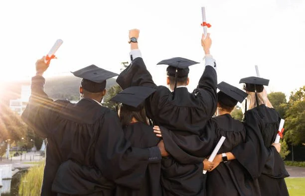 Group of graduates in caps and gowns holding diplomas during outdoor graduation ceremony