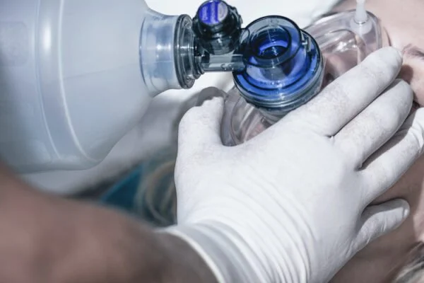 Close-up of a person receiving CPR with a bag-valve mask, wearing gloves.