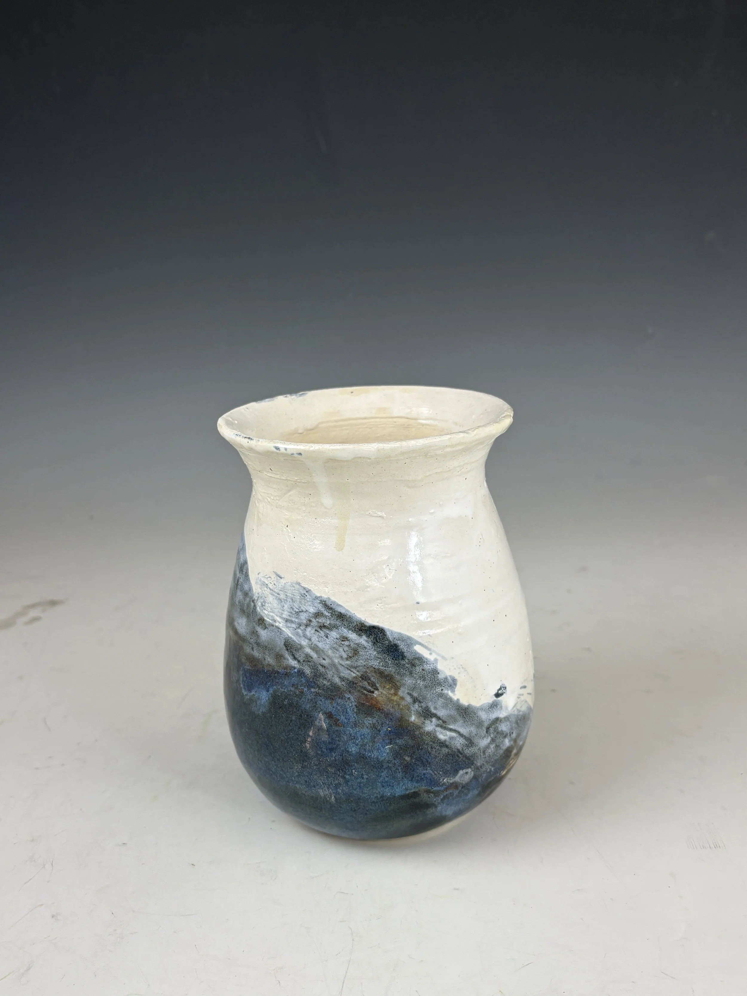 Ceramic vase with mountain design, white upper half, dark blue and gray lower half, against a gradient background.