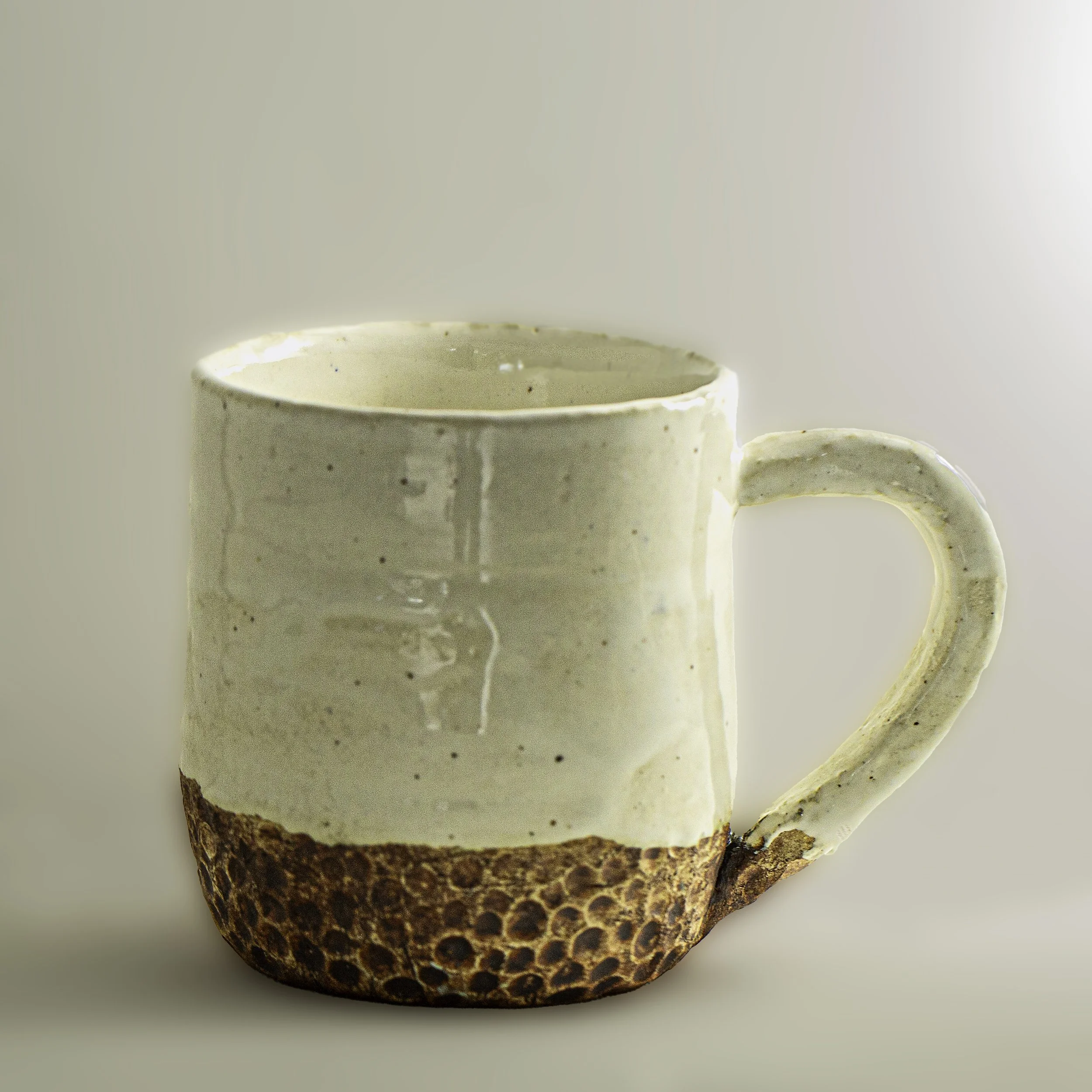 A ceramic mug with a textured brown bottom half and cream-colored top half, set against a plain background.