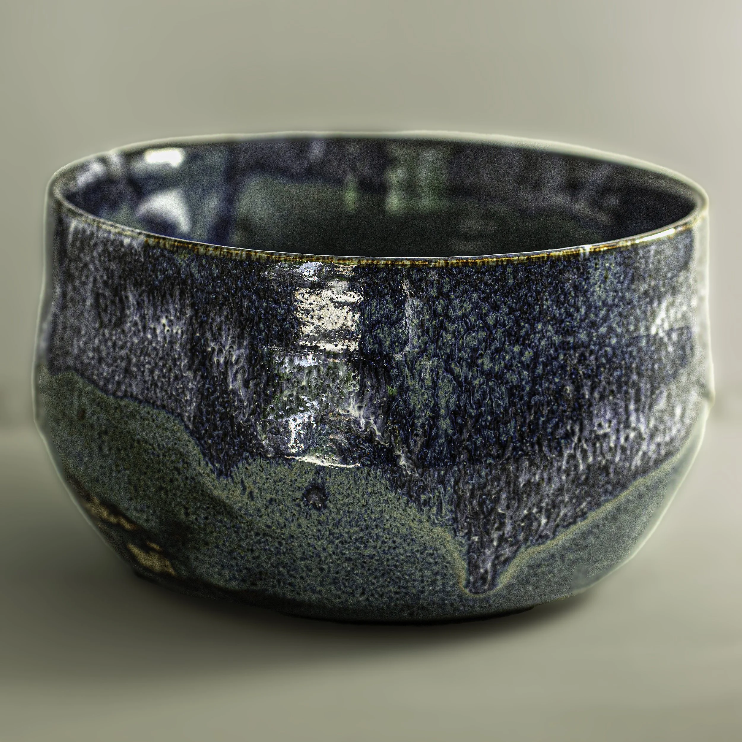 Close-up of a ceramic bowl with a textured, glossy glaze in shades of blue, green, and black.
