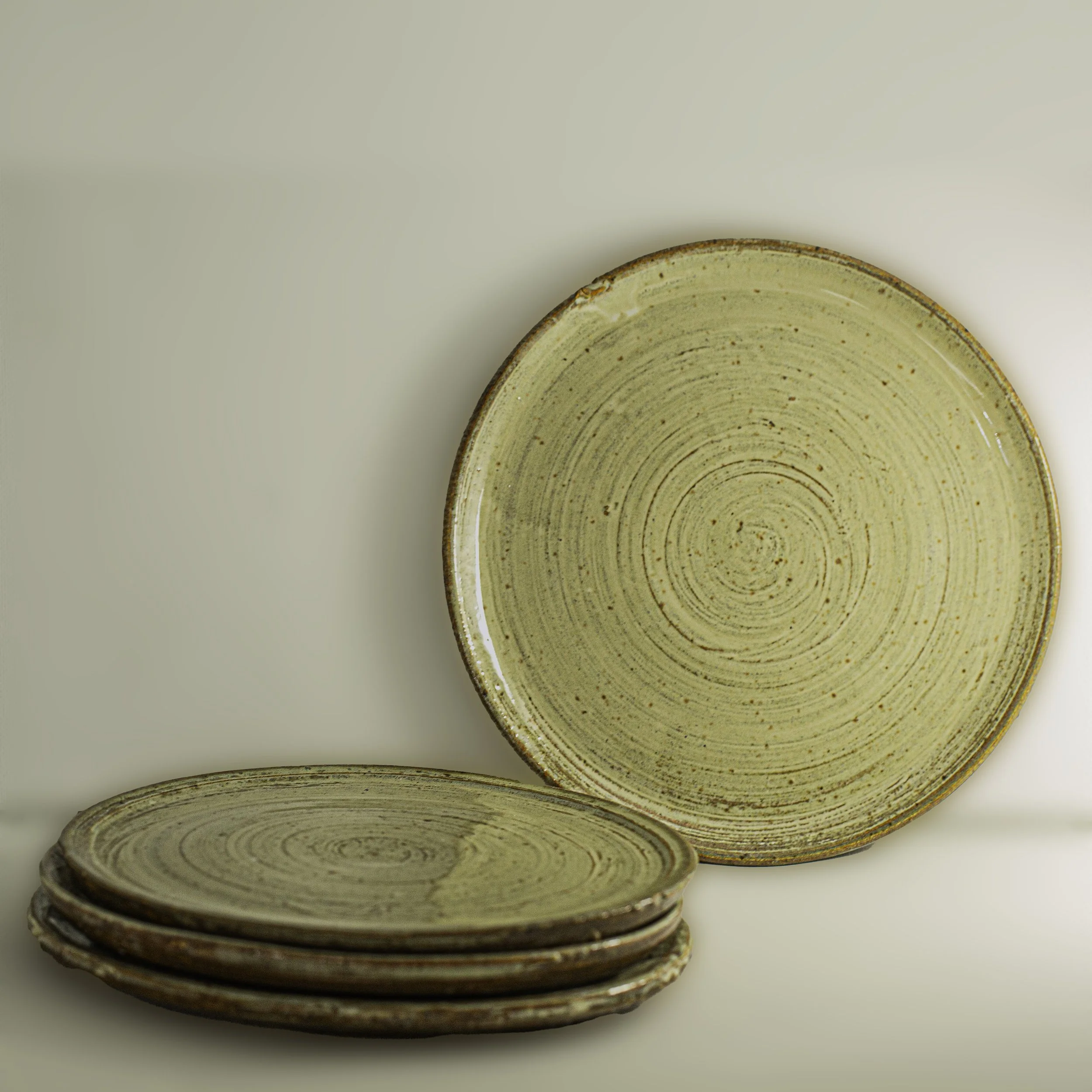 A set of ceramic plates with a beige glaze and circular spiral patterns, with some stacked and one placed upright.