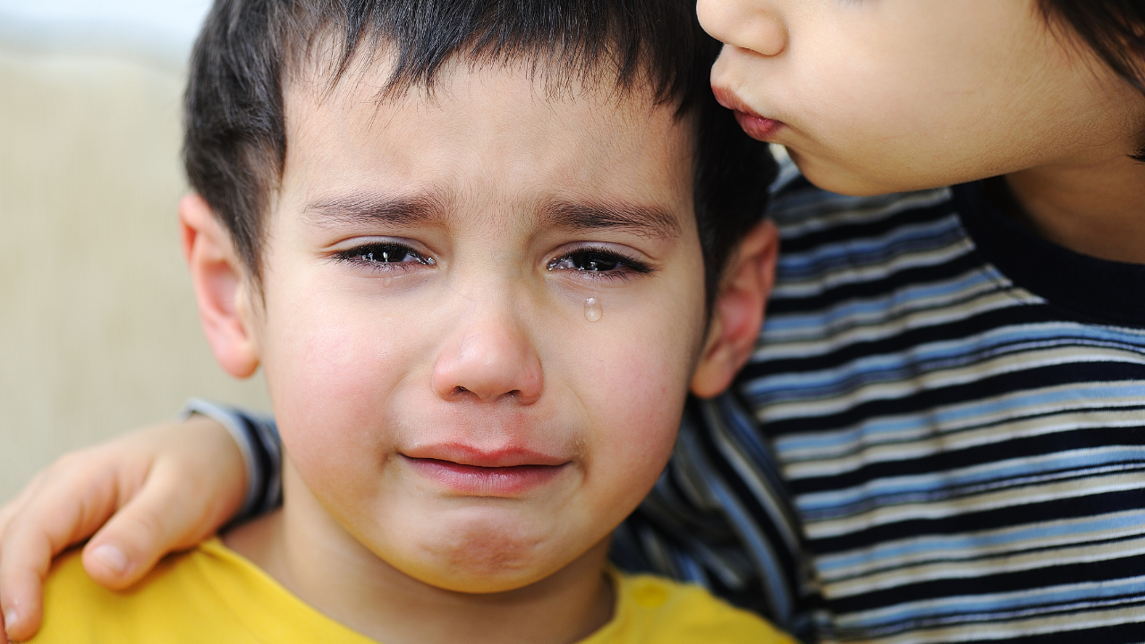 A young boy crying with tears on his face, comforted by another child leaning in close.