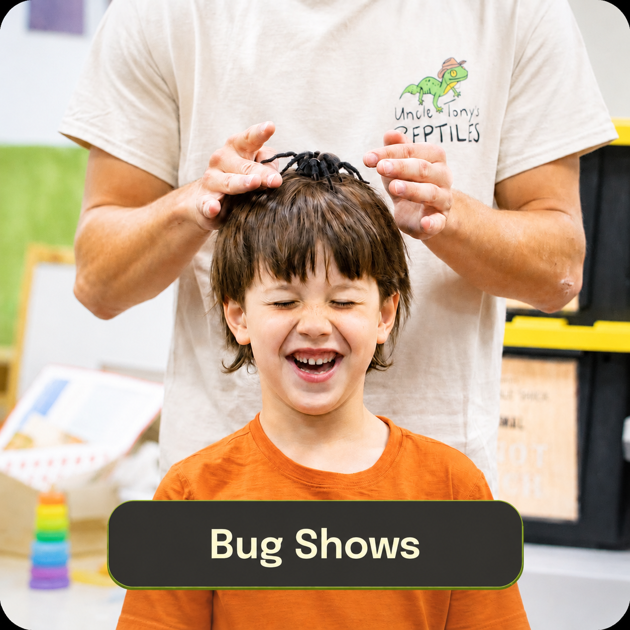 A young boy with brown hair and an orange shirt laughing while a person behind him places a plastic spider on his head. The person is wearing a beige t-shirt with a green lizard and the text 'Uncle Tony's Reptiles.' A sign at the bottom reads 'Bug Shows.'