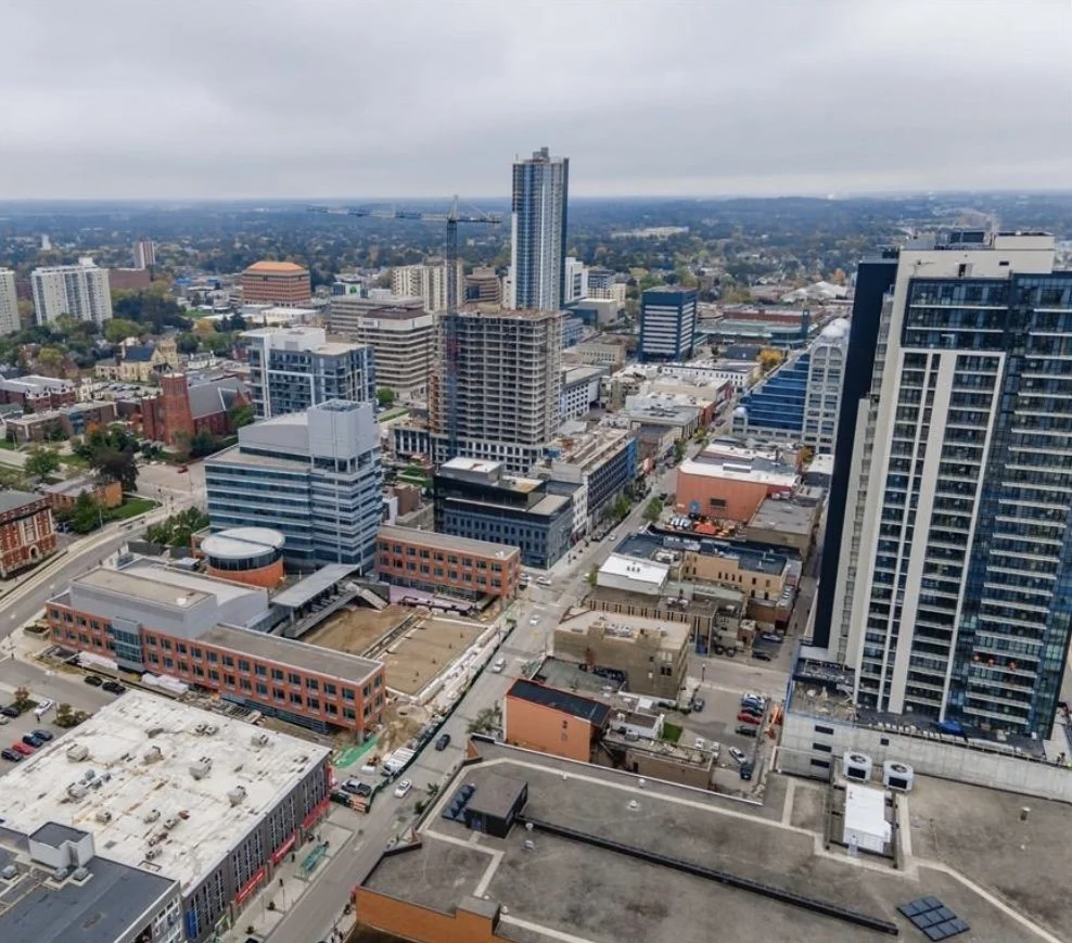 A cityscape showing tall buildings and skyscrapers in a downtown area with some construction cranes and a cloudy sky.