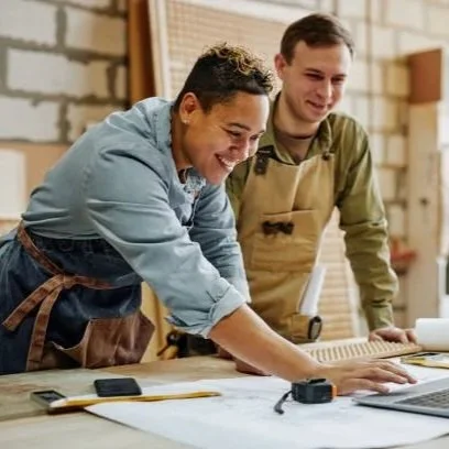 Two people working together at a table, smiling, with tools and papers around.