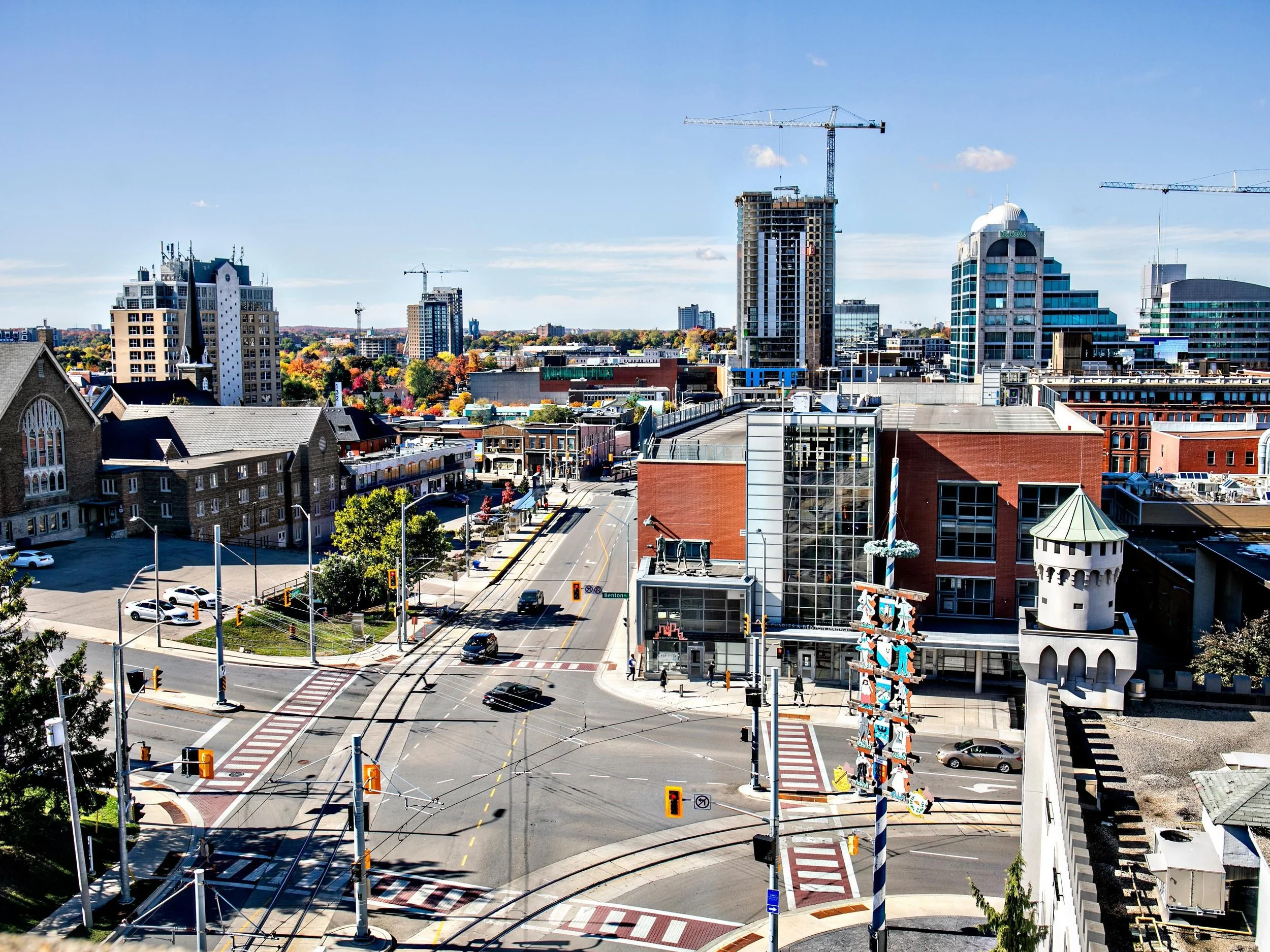 Cityscape with streets, cars, buildings, construction cranes, and a partly cloudy sky.