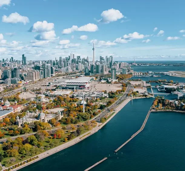 Aerial view of Toronto skyline with CN Tower, Lake Ontario, and city parks with fall foliage.
