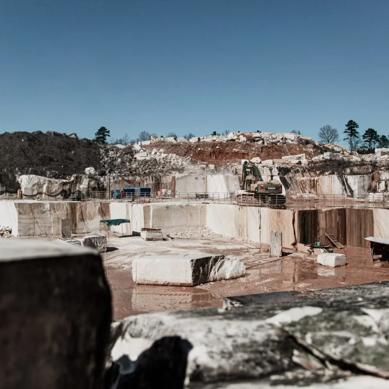 A large open-pit quarry with white stone blocks, construction equipment, and fencing under a clear blue sky.