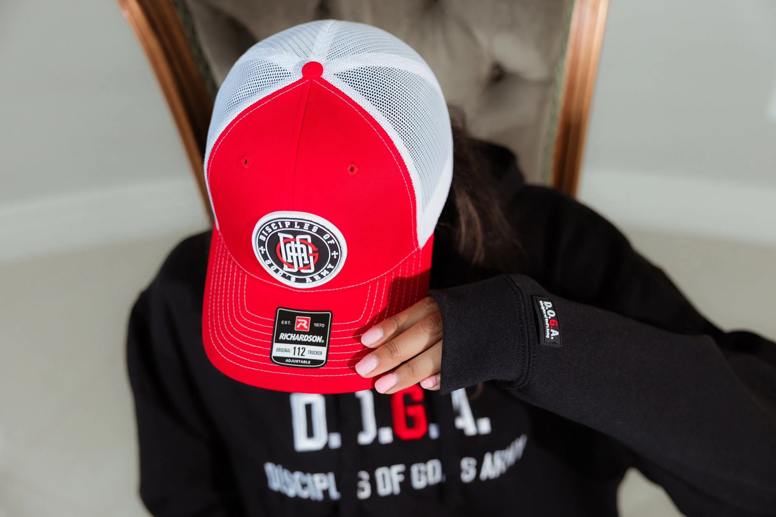 A black hoodie with a Disciples of God's Army logo. A red and white trucker hat with a 3D PVC Rubber logo on the front.