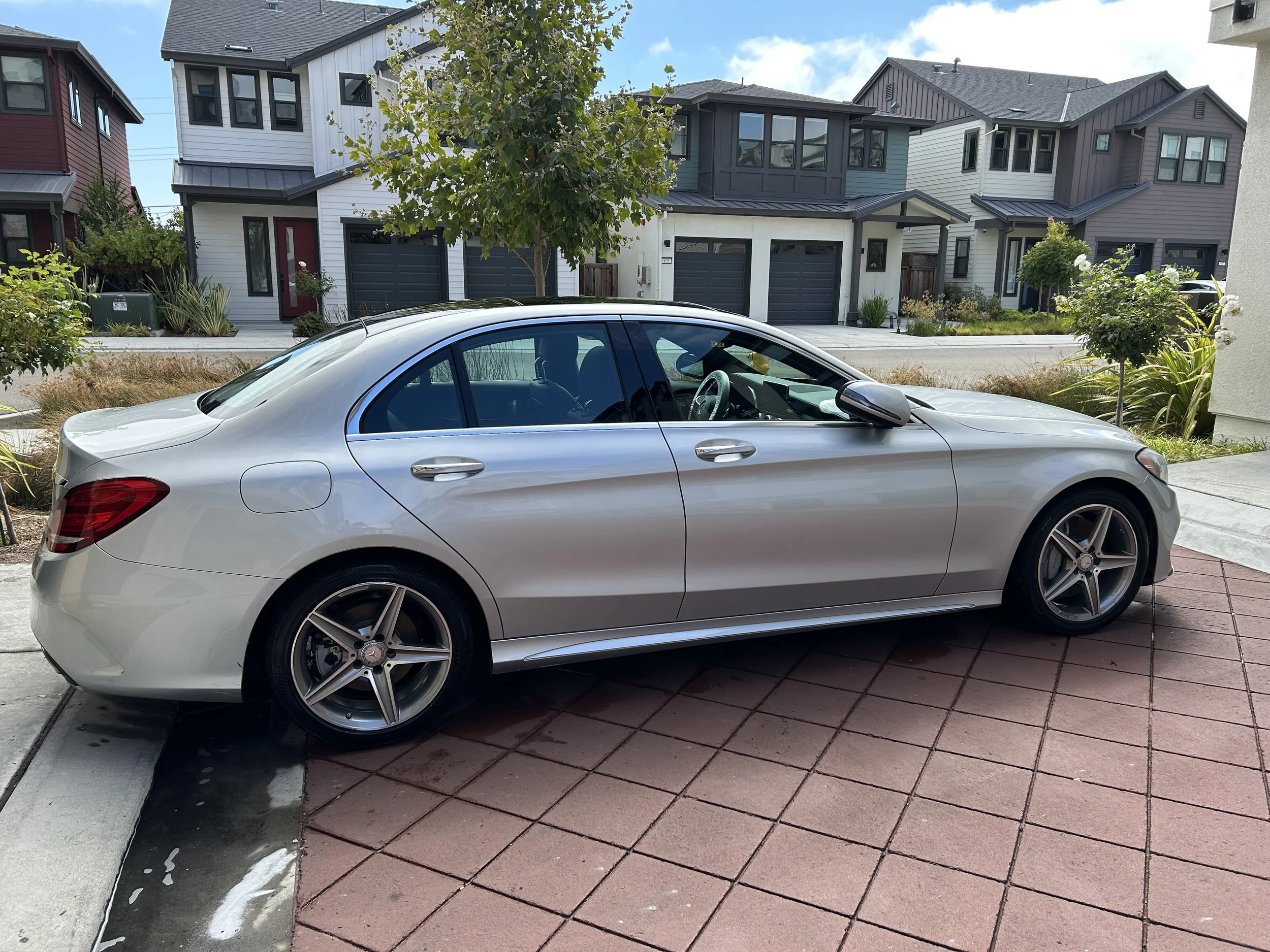 Silver Mercedes-Benz sedan parked in a driveway with modern houses in the background.