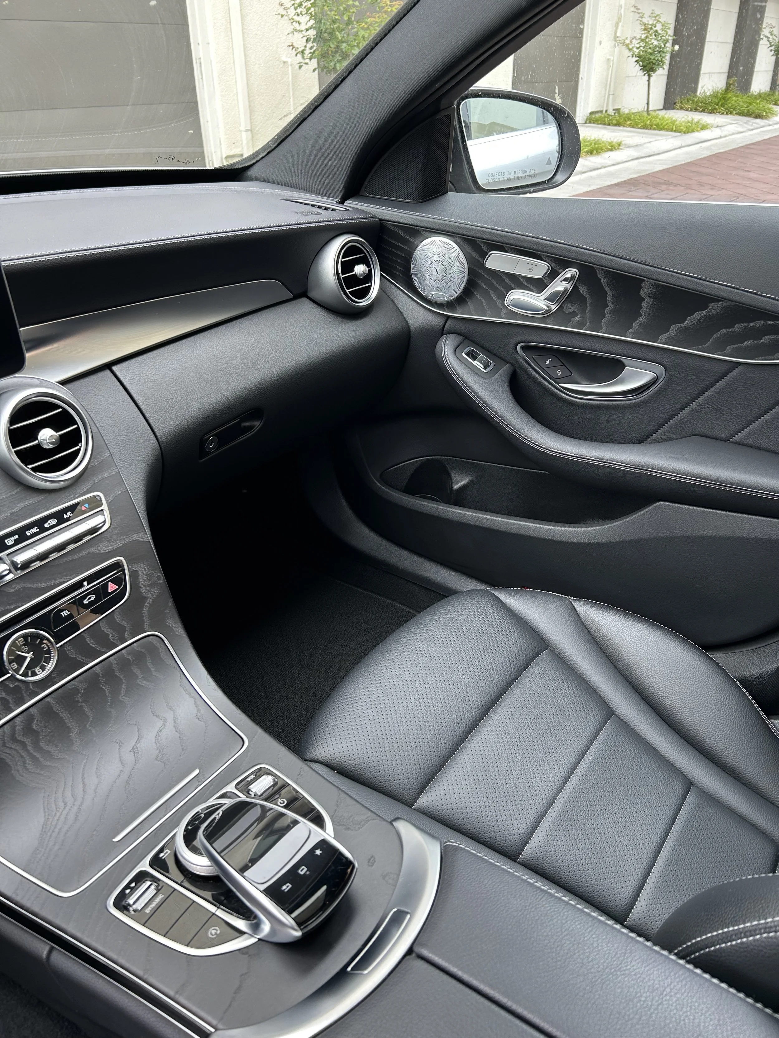 Interior of a modern car showing the driver's side, dashboard, air vents, control buttons, and a seat in black leather with white stitching.