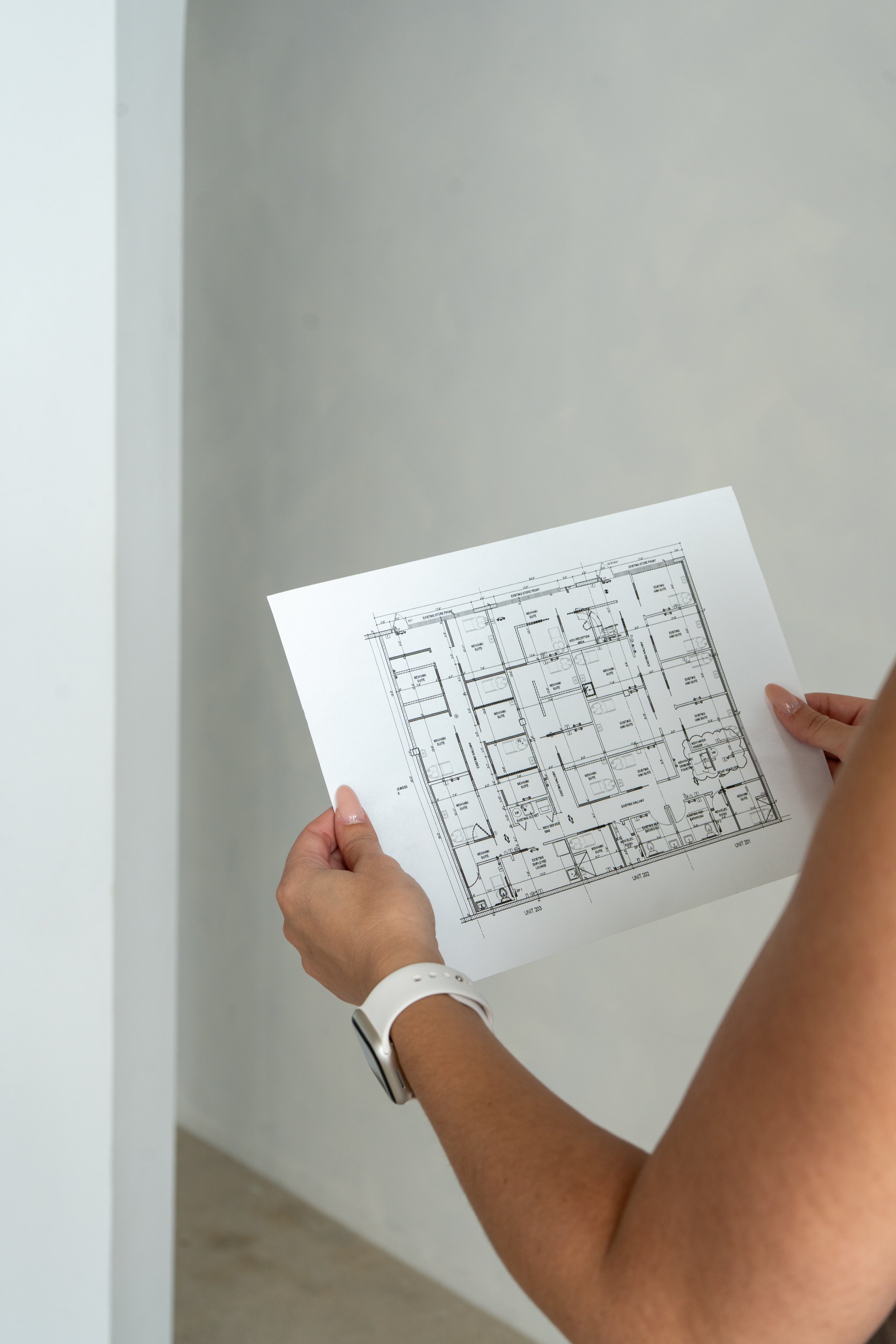 Person holding detailed architectural blueprint in a room with plain white and gray walls