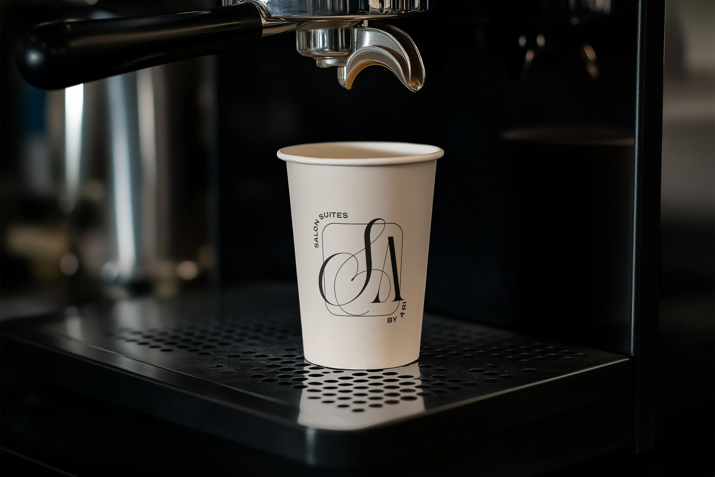 A white disposable coffee cup on a black coffee machine drip tray with a black spout above.