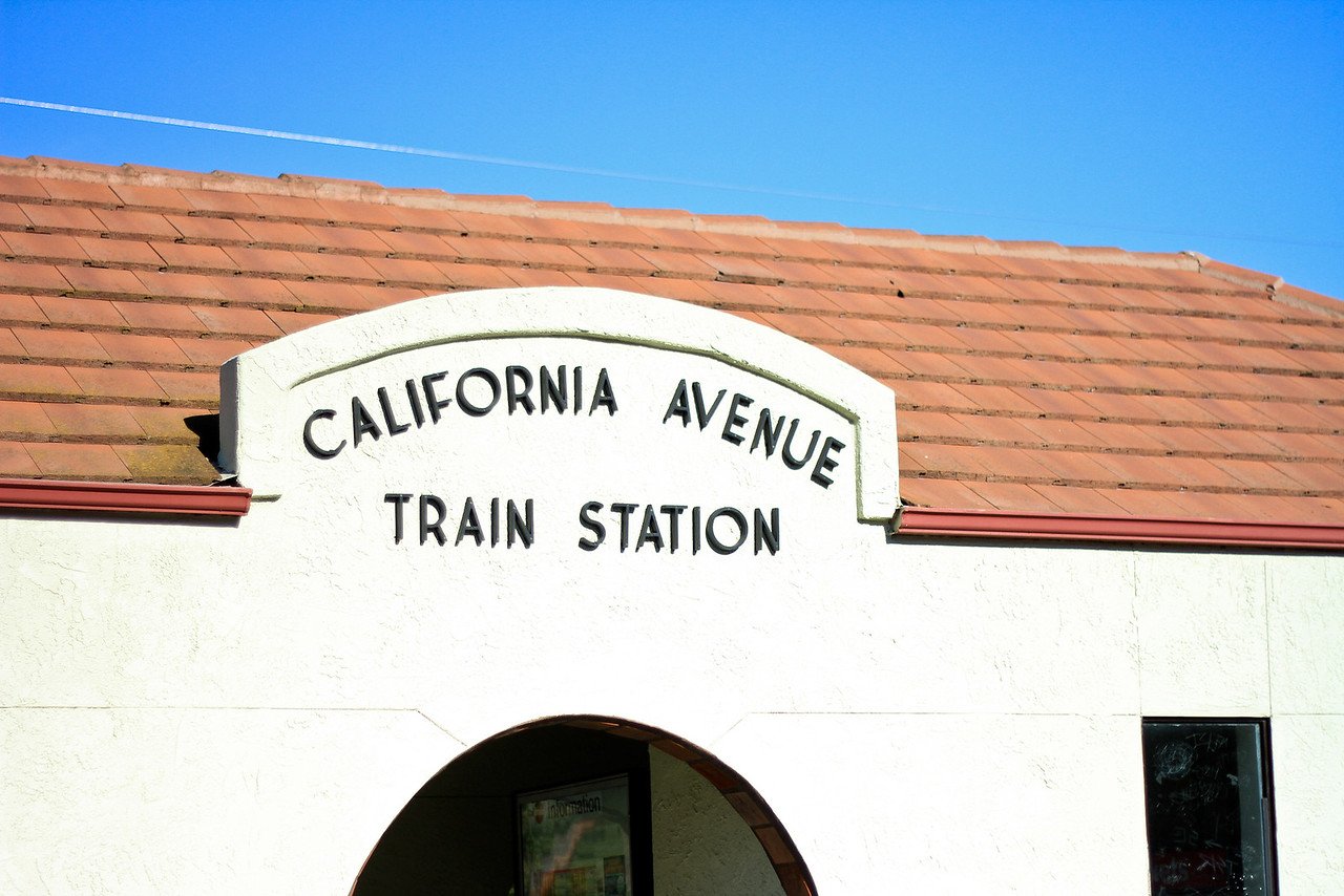 Sign that reads 'California Avenue Train Station' on a building with a red-tiled roof and a clear blue sky.