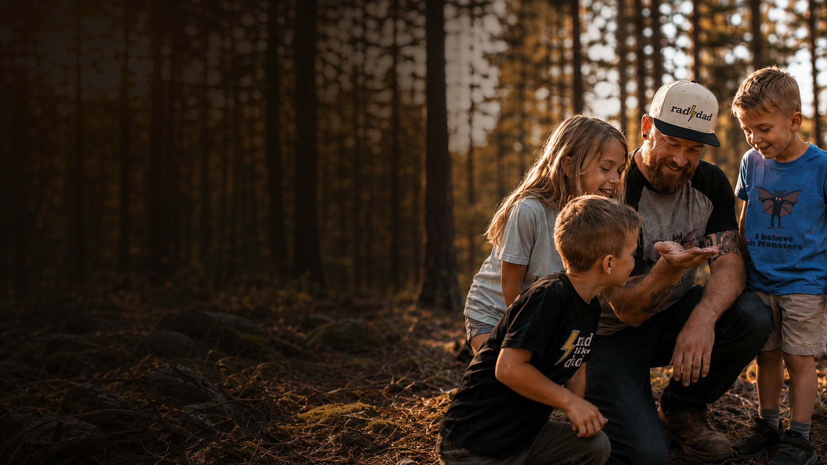A man with a beard and tattoos wearing a baseball cap with the word 'rad' and lightning bolt logo, surrounded by four children in a forest during sunset, all looking at a phone.