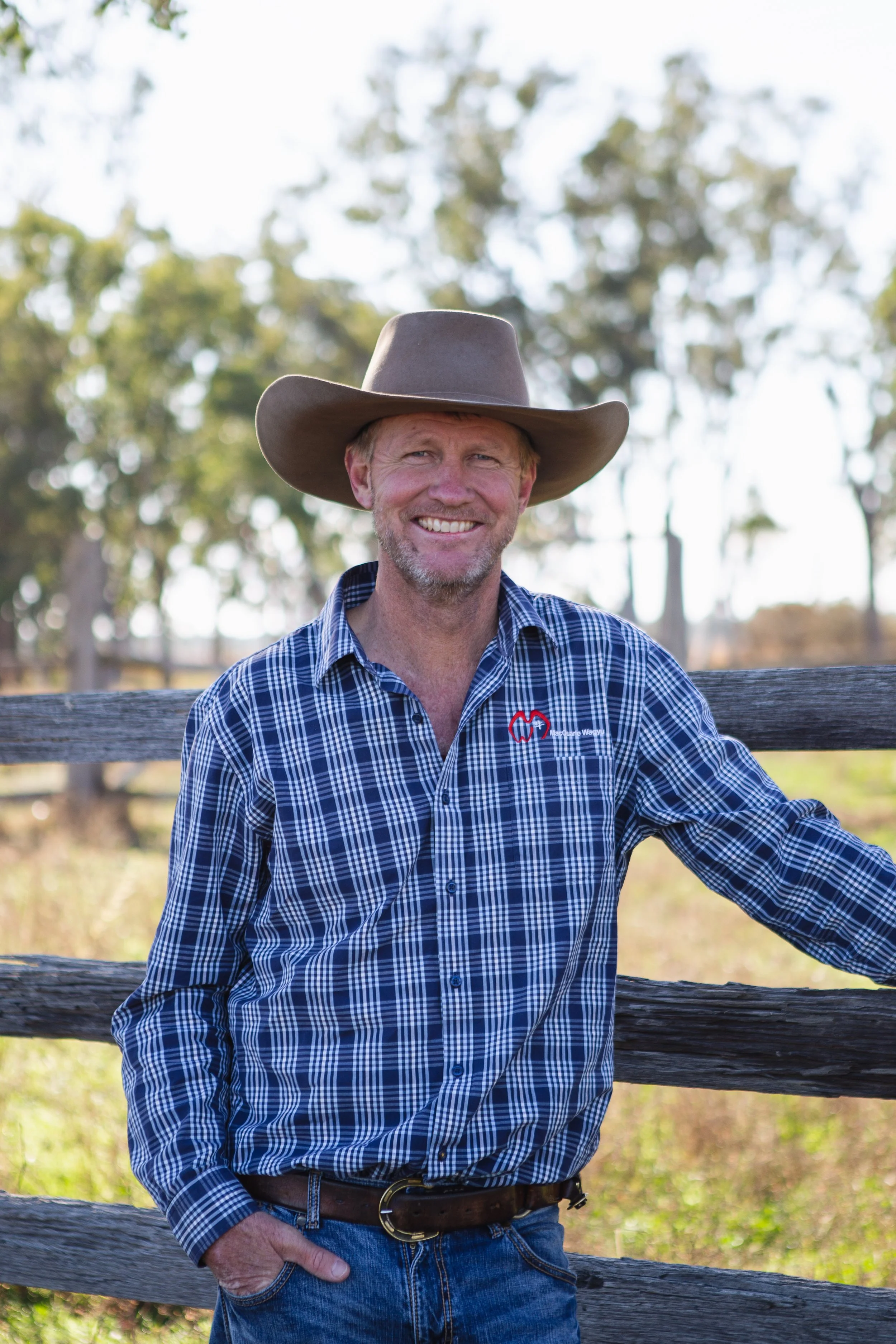 man standing against wooden fence smiling with hat on