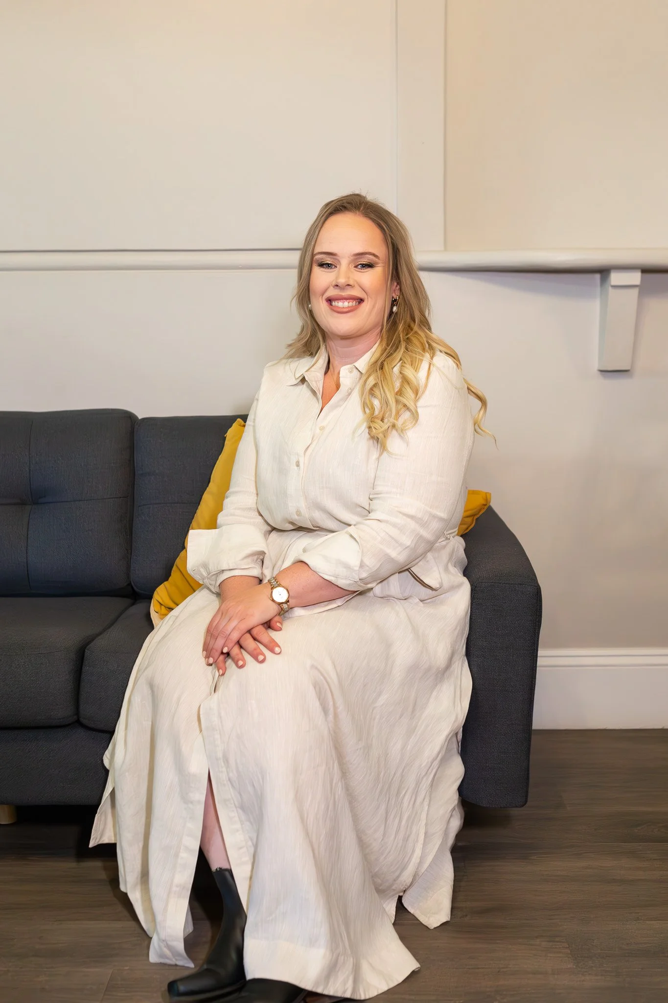 woman sitting on lounge clasping hands and smiling in wheaten linen dress