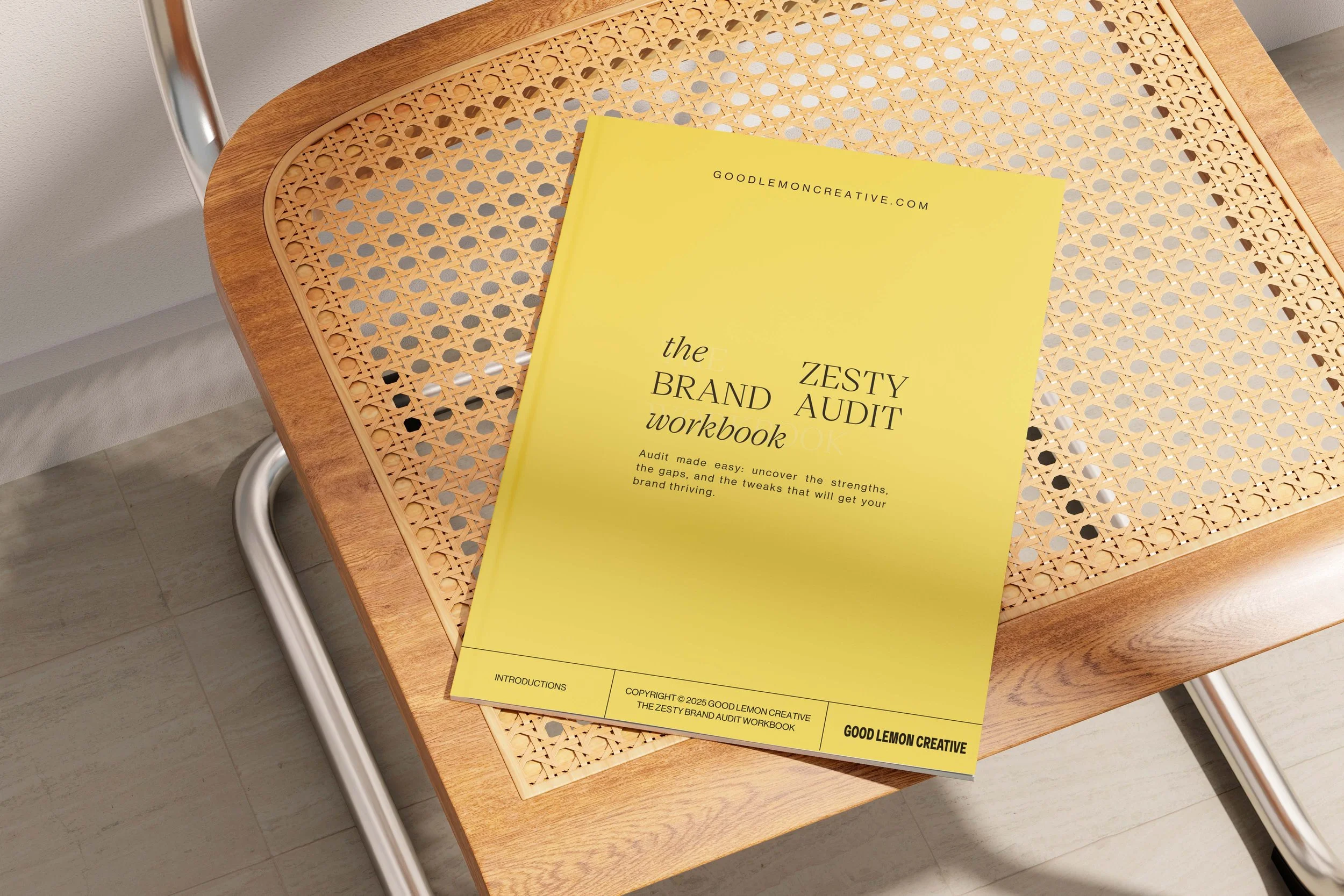 Yellow brand audit workbook titled 'Zesty Brand Audit Workbook' resting on a wooden table with a woven cane top, near a silver metal chair.