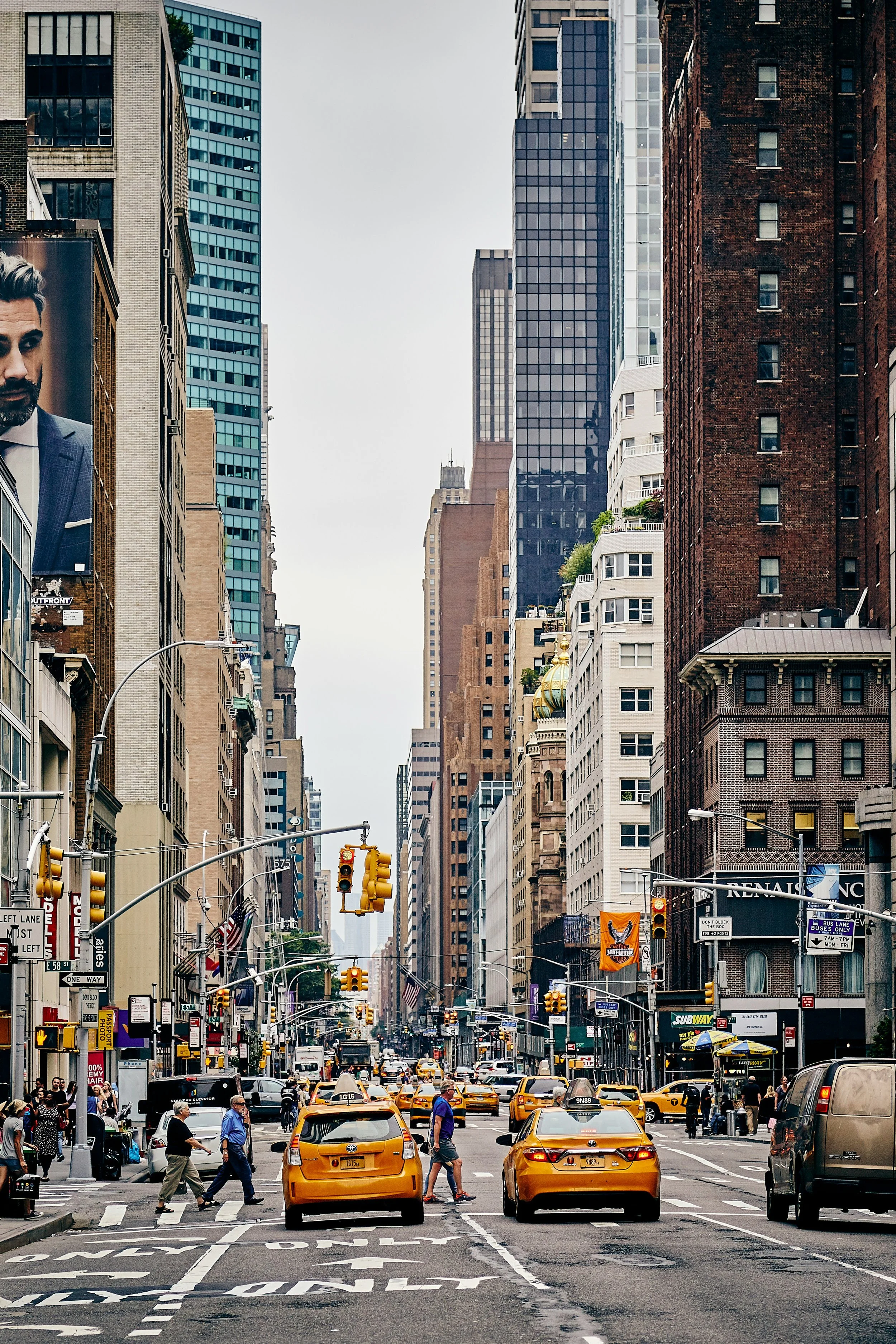 A busy city street in Manhattan, New York City, with yellow taxis, pedestrians, tall skyscrapers, and traffic lights.