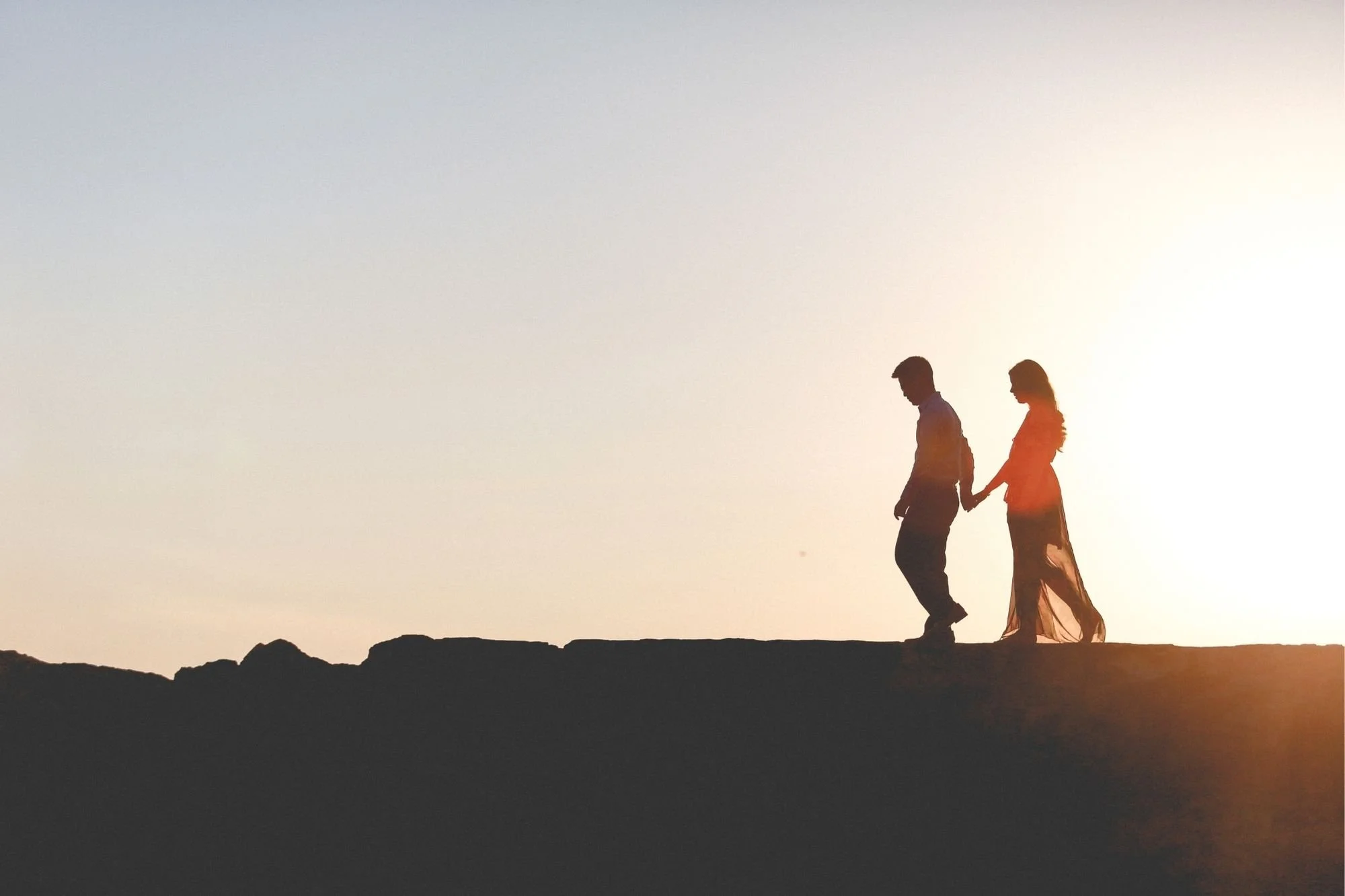 Silhouettes of a couple, a man and woman holding hands on a hill during sunset