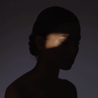 Silhouette of a woman's profile with dramatic lighting highlighting only part of her face and hair.