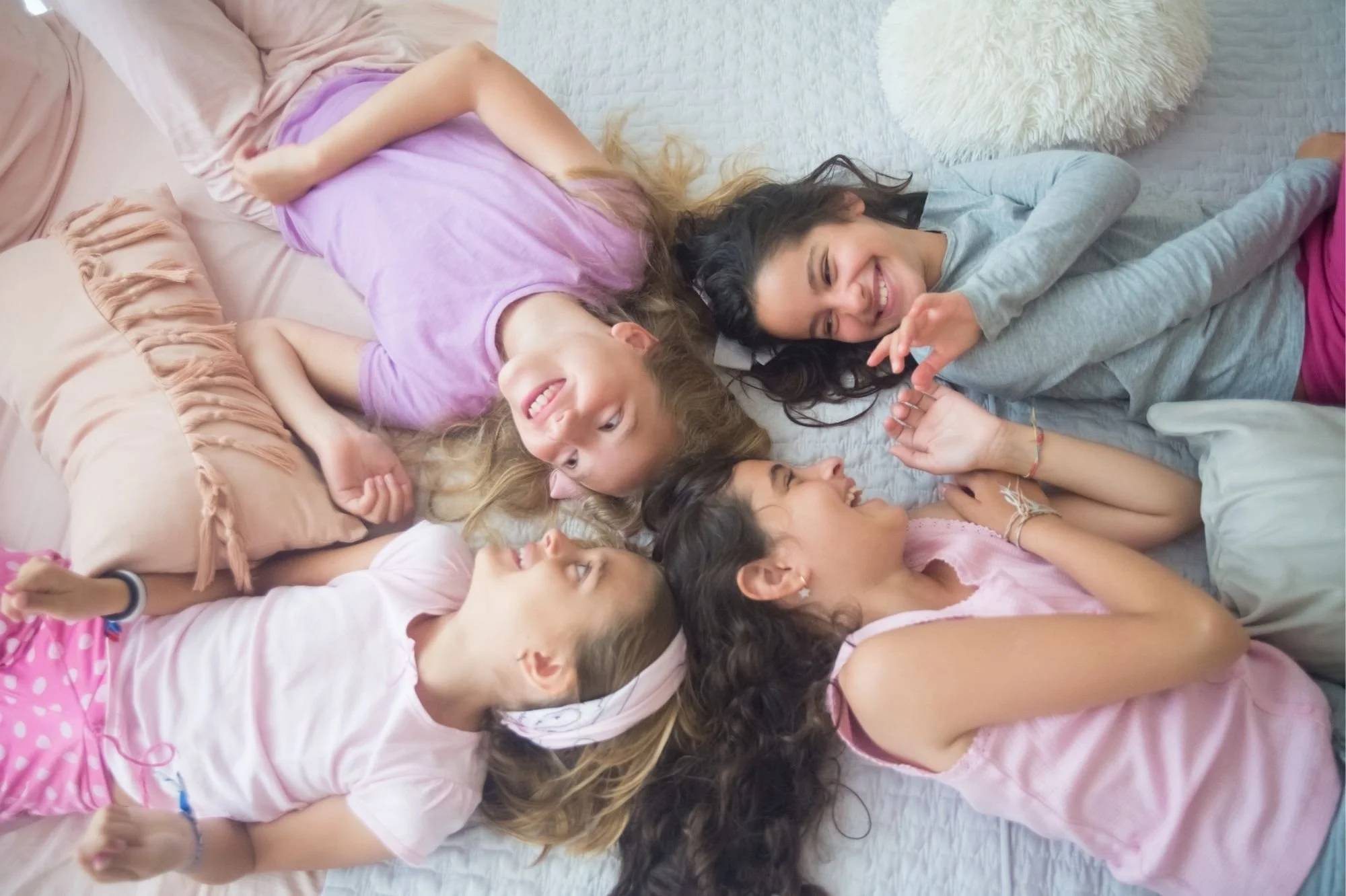Four young girls lying on a bed, smiling and talking with each other.