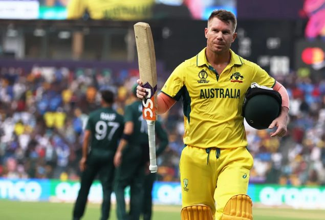Australian cricket player walking off the field holding a bat and helmet after a match, with spectators and other players in the background.