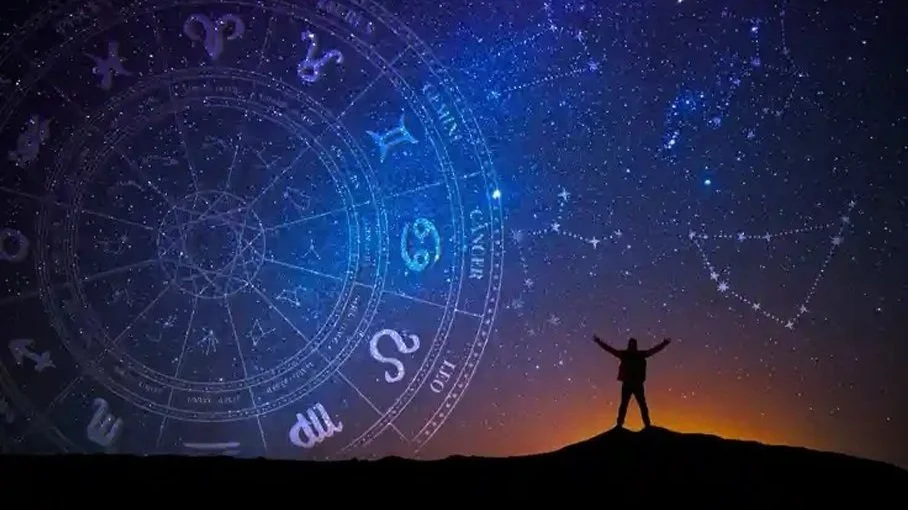 A silhouette of a person standing on a hill with arms raised, under a night sky filled with stars and astronomical constellations, and a large transparent zodiac wheel overlay.