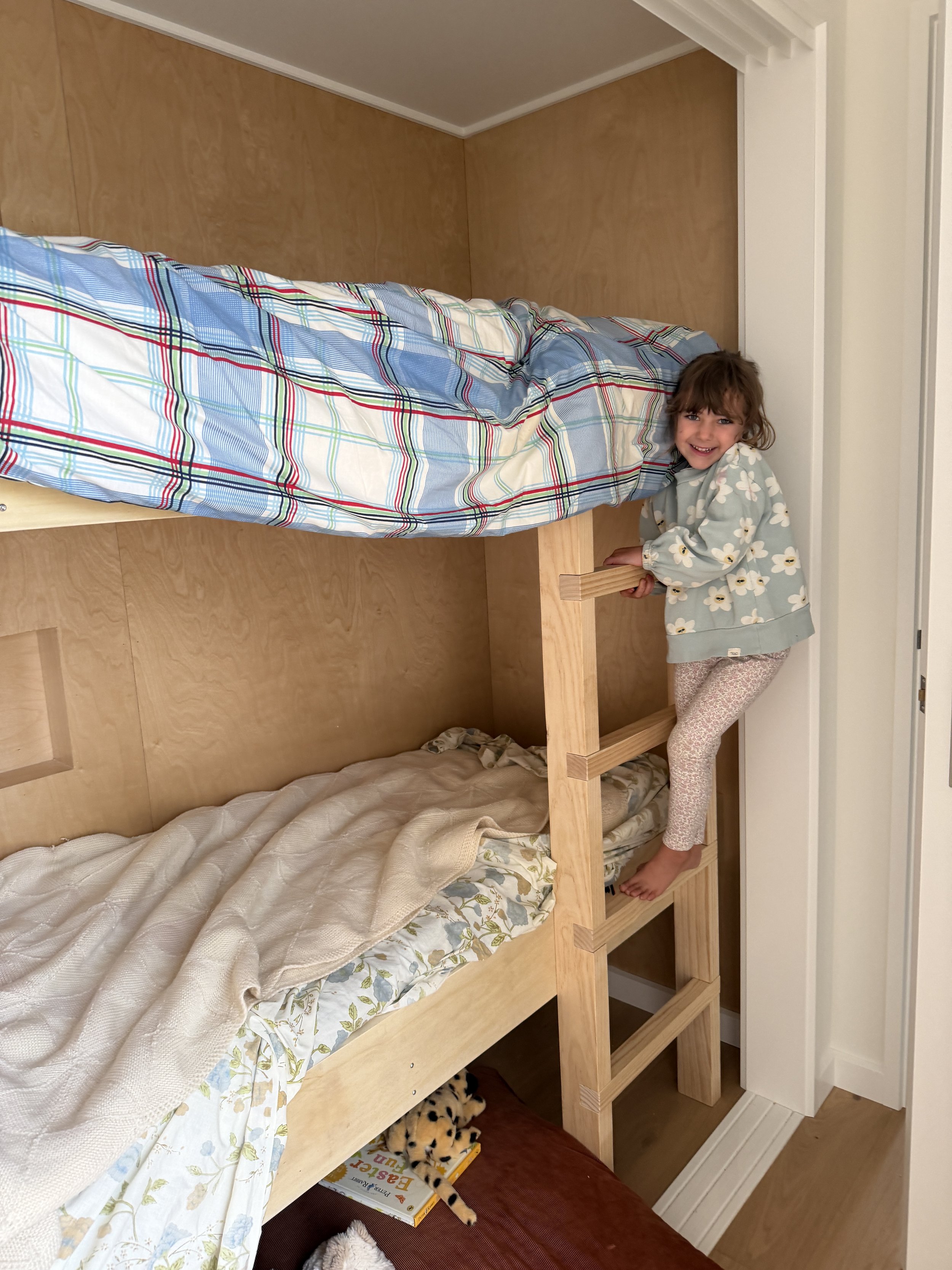 A young girl with curly hair standing beside the bunk beds, a clever design addition for extra capacity in this home near Clyde, Central Otago. Designed to maximise space by Candela Architecture