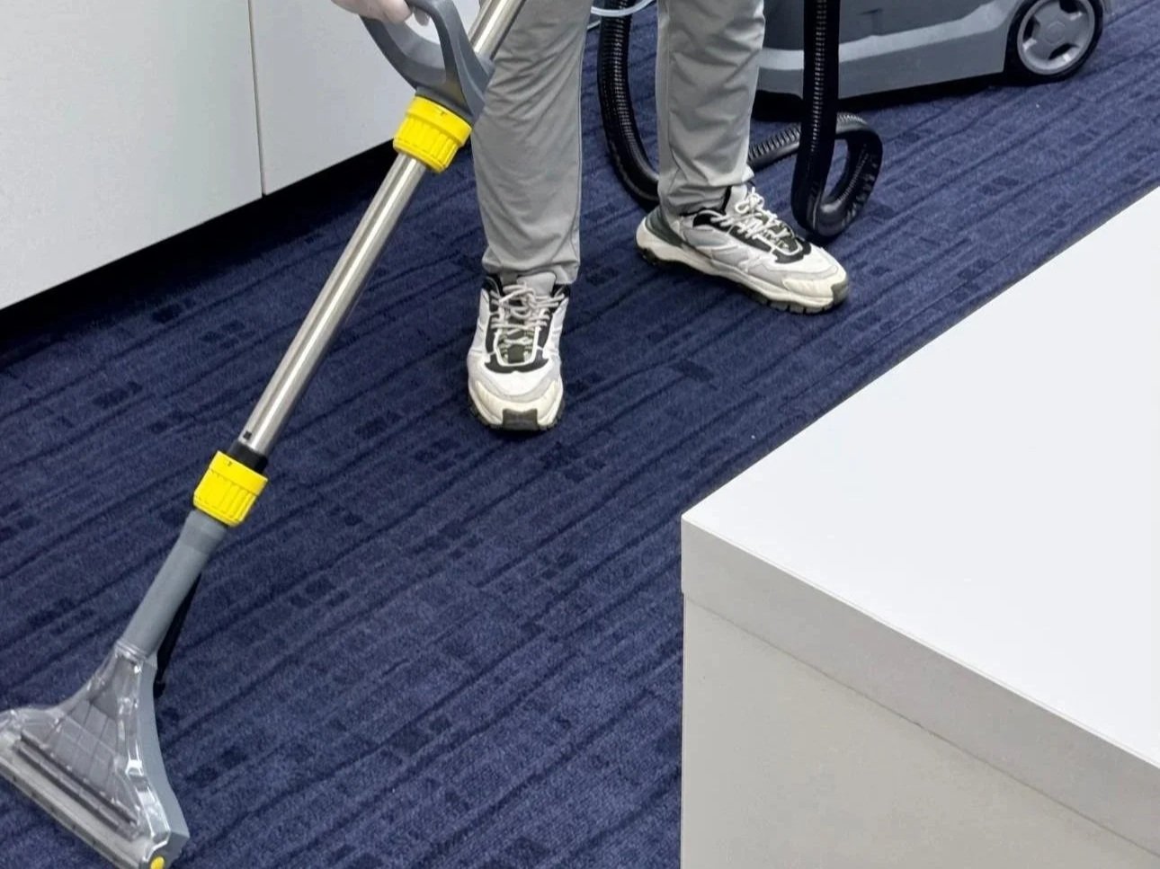 Person cleaning carpet with a vacuum cleaner in an indoor setting.