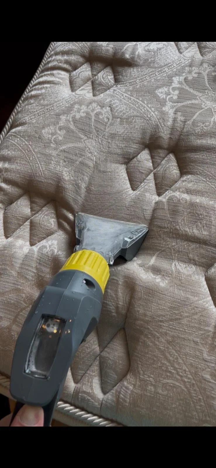 A hand holding a handheld steam cleaner on a vintage patterned fabric upholstery, removing wrinkles and creases.