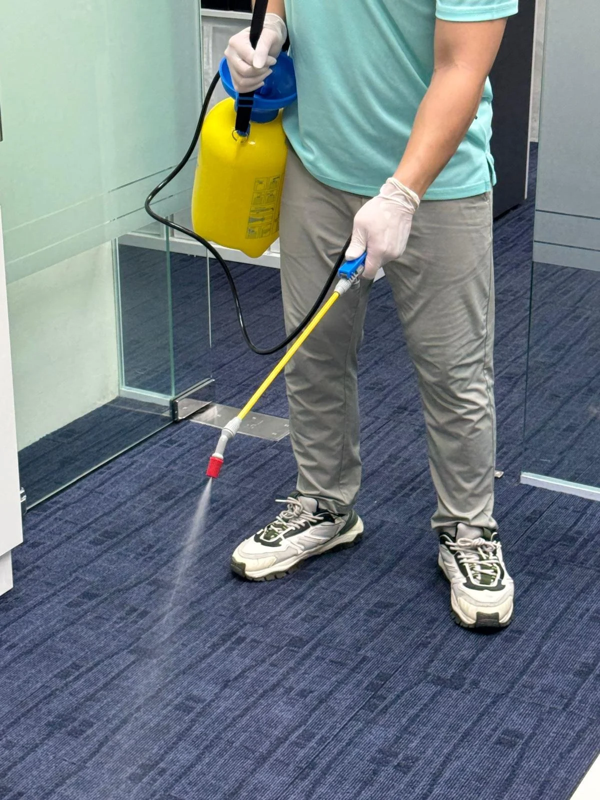 Person wearing gloves spray disinfection on carpeted floor in an office building.
