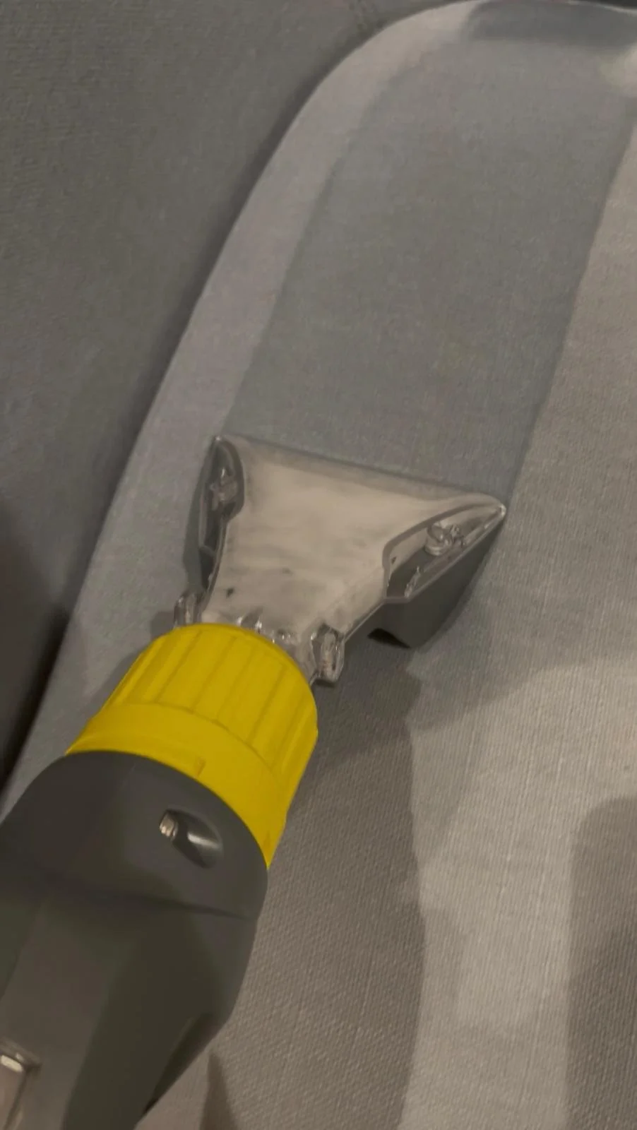 Close-up of a handheld vacuum cleaner with a yellow and gray body cleaning a gray fabric surface.