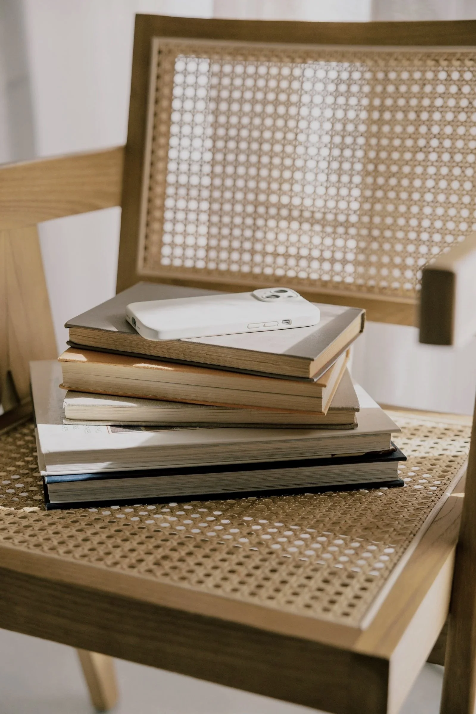 A stack of six books on a woven rattan chair with a white smartphone placed on top.