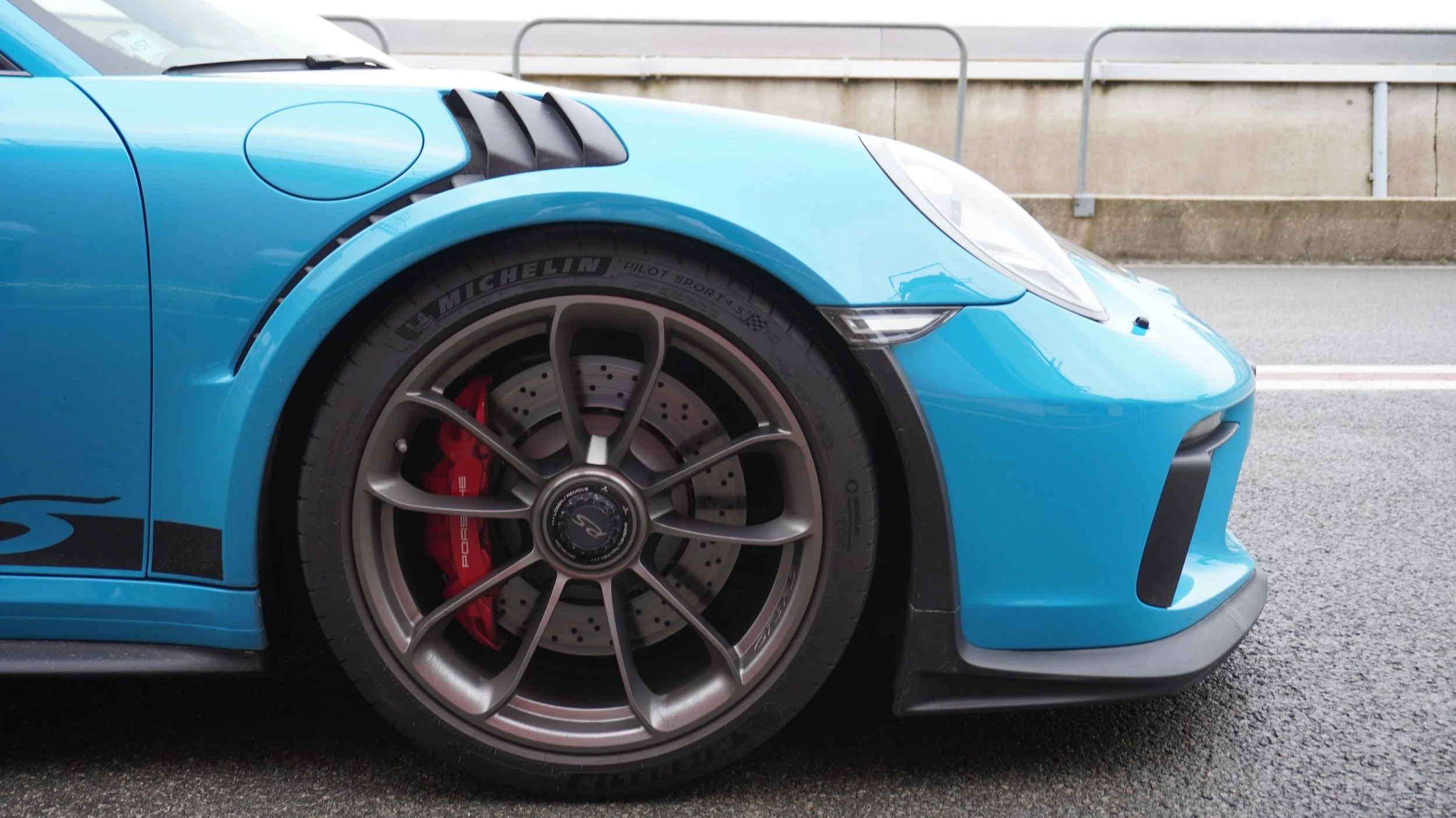 Close-up van de voorkant van een blauwe Porsche sportauto, met een zichtbaar rood remblok en Michelin banden.