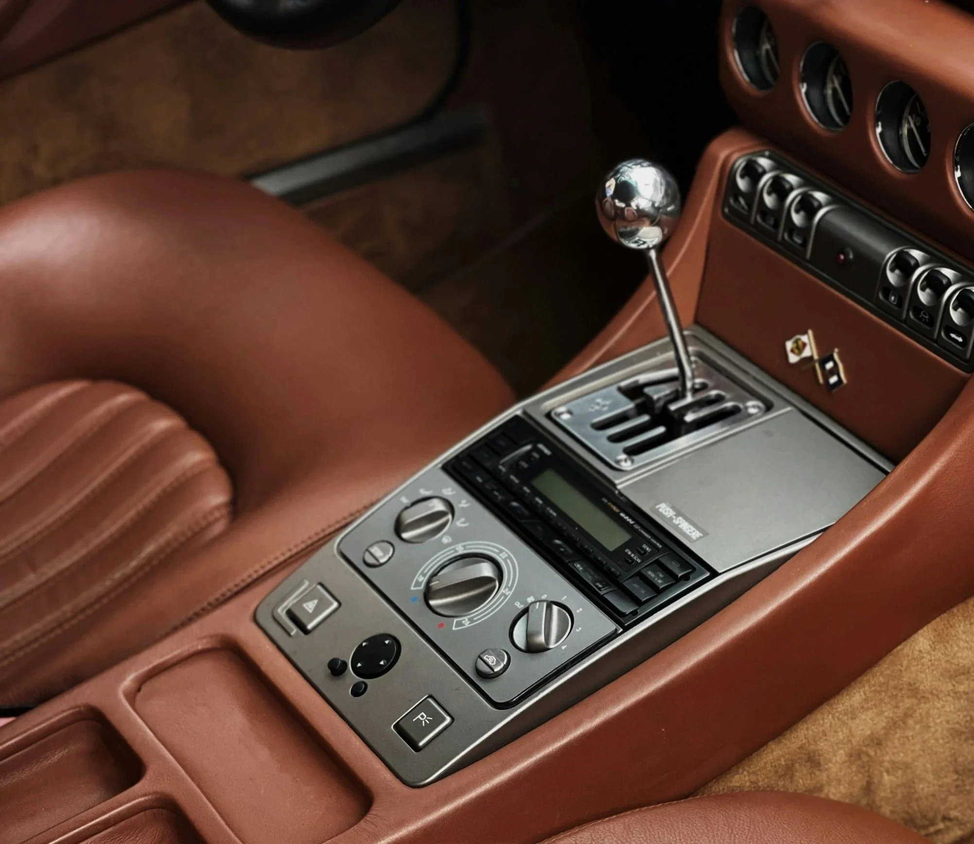 Interieur van een auto met een manuele versnellingsbak, een dashboard met ventilatieopeningen en een radio, bekleed met bruin leder.