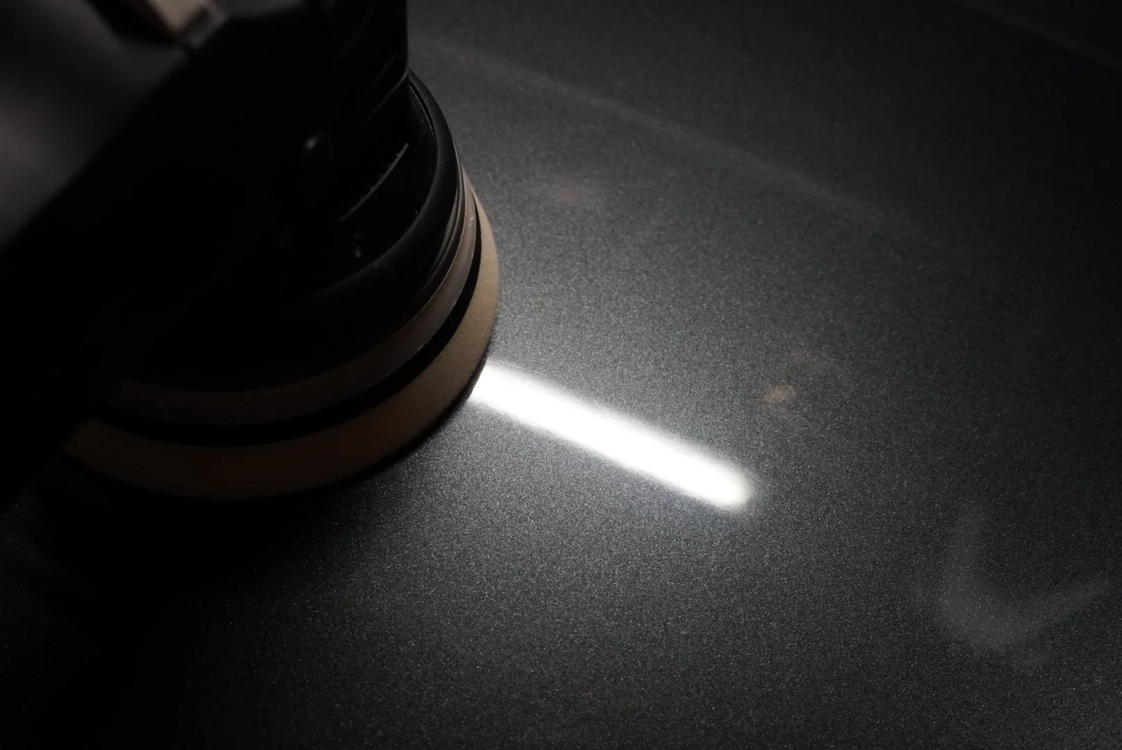Een polijstmachine die over een metalen oppervlak beweegt, waardoor een reflectie van een lichtlijn ontstaat.