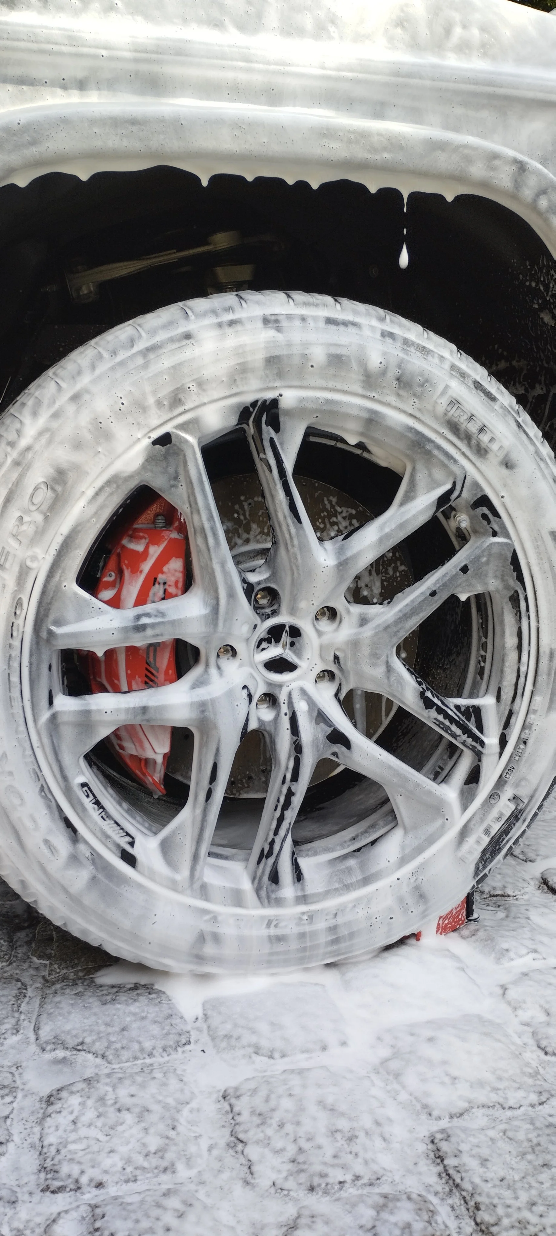 Wielen van een auto bedekt met zeep tijdens het wassen op een gewelfd betonnen oppervlak.