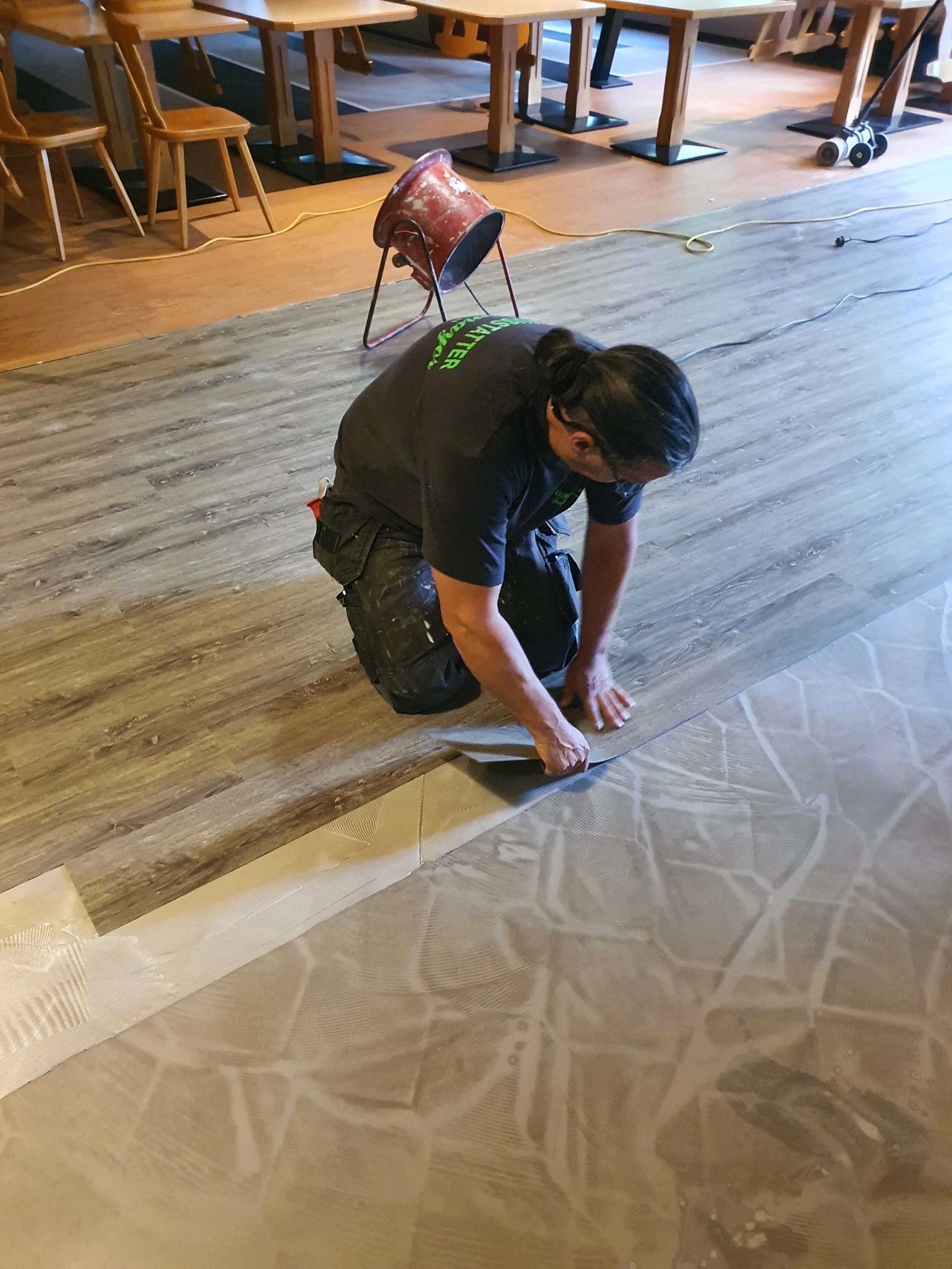 Mitarbeiter verlegt sorgfältig einen Bodenbelag – professionelle Handwerksarbeit bei der Raumausstattung