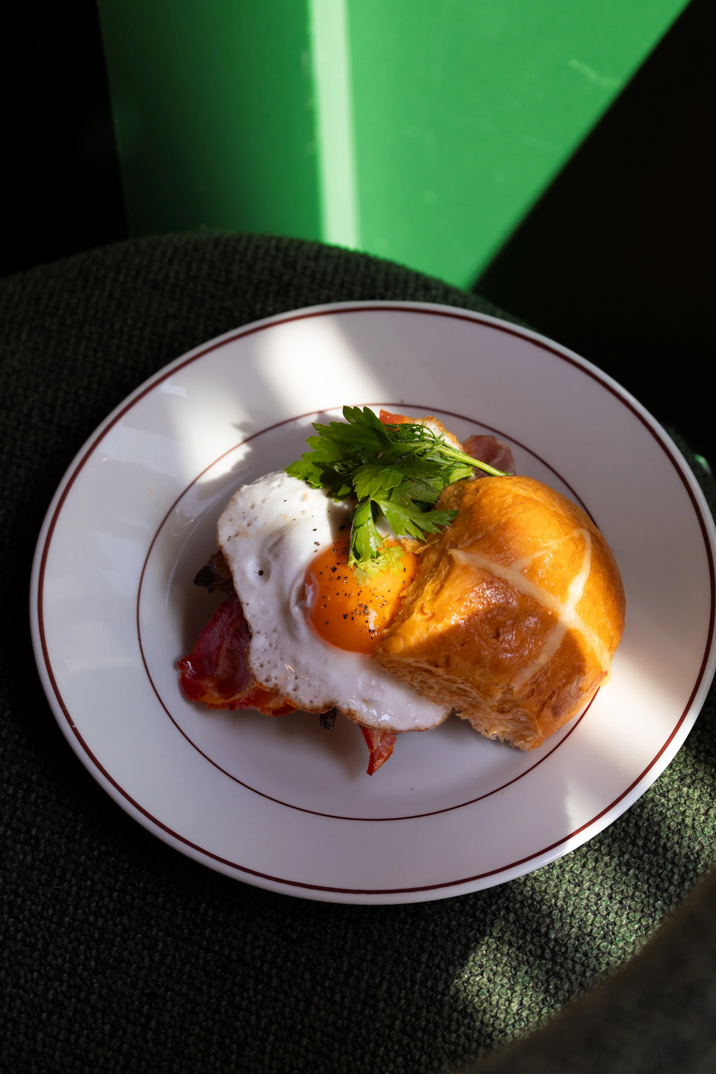 Bun avec oeuf au plat et bacon sur tabouret avec ombre et lumière