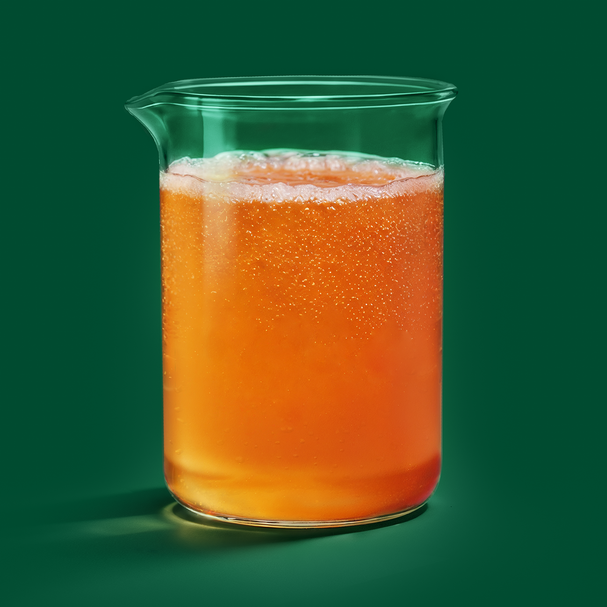 A close-up of a glass of iced orange-colored kombucha cocktail with ice cubes.