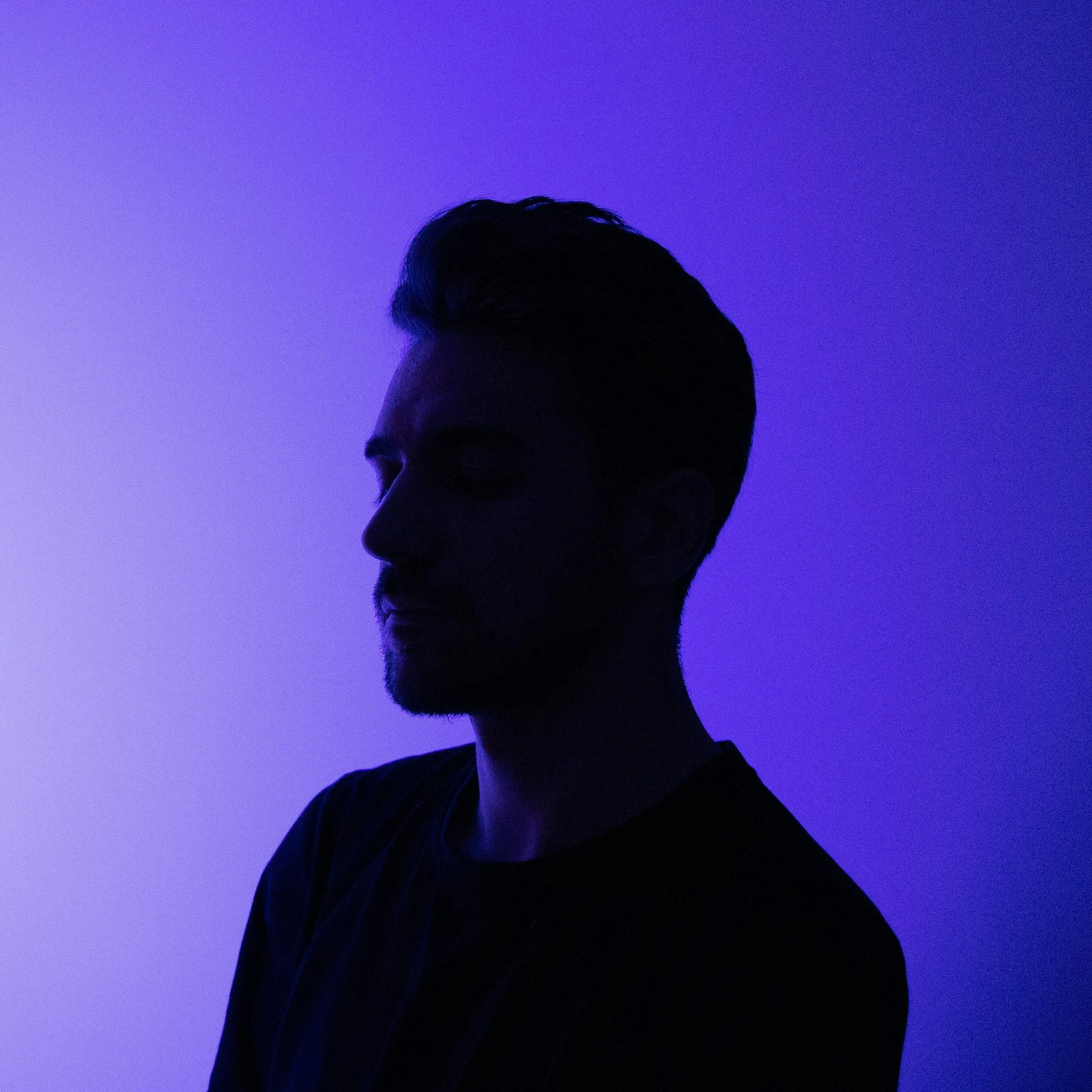 Silhouette of a man with styled hair, facing left, against a purple and blue gradient background.