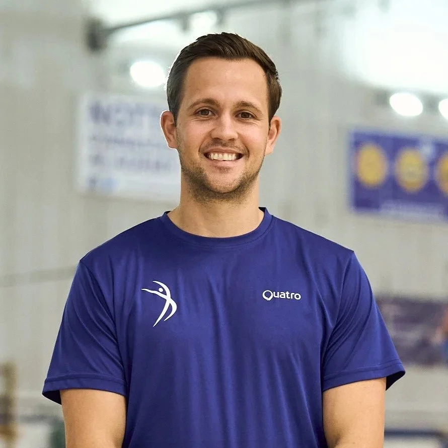 A smiling young man in a blue athletic shirt standing indoors.