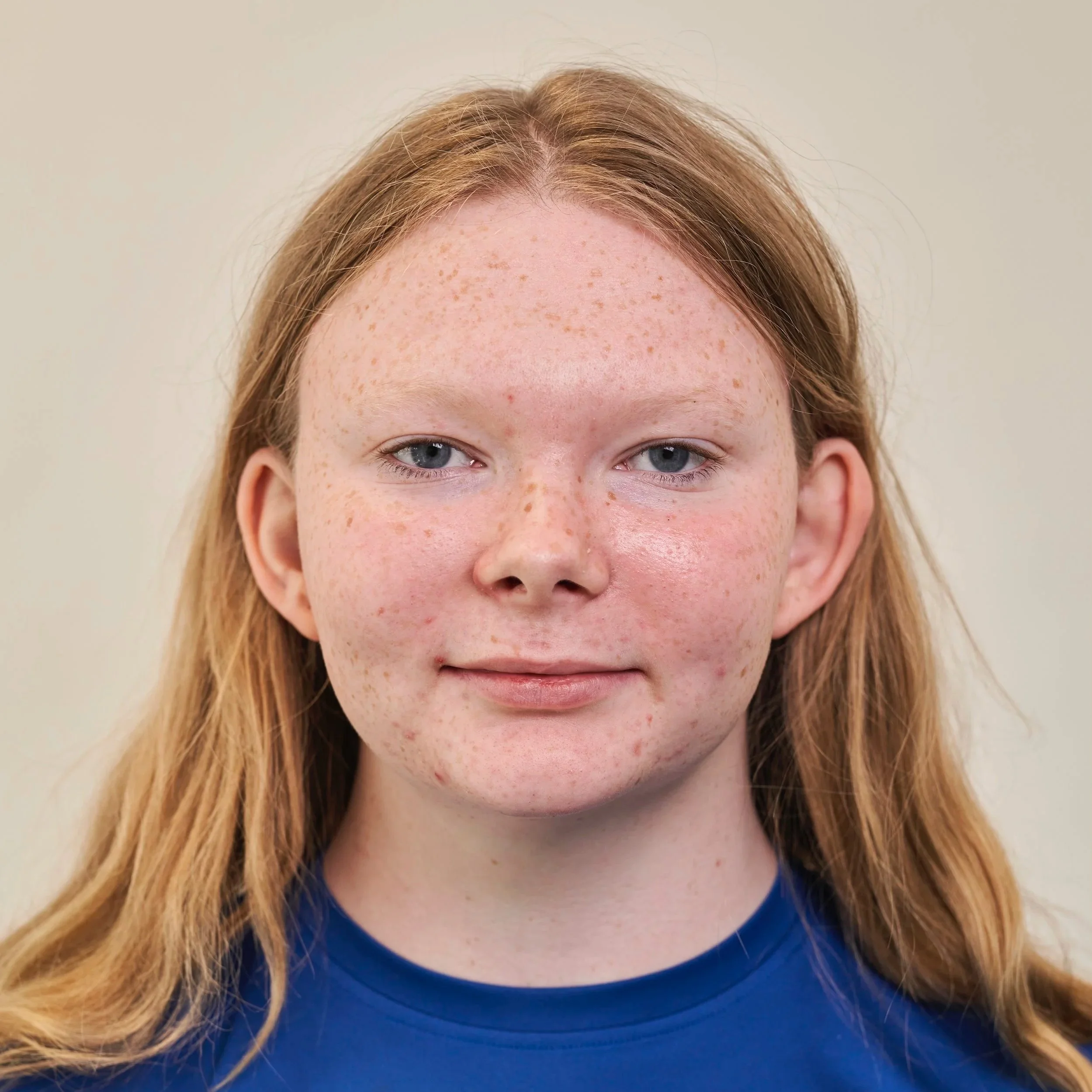 Close-up of a young girl with red hair and freckles, wearing a blue shirt, smiling slightly.