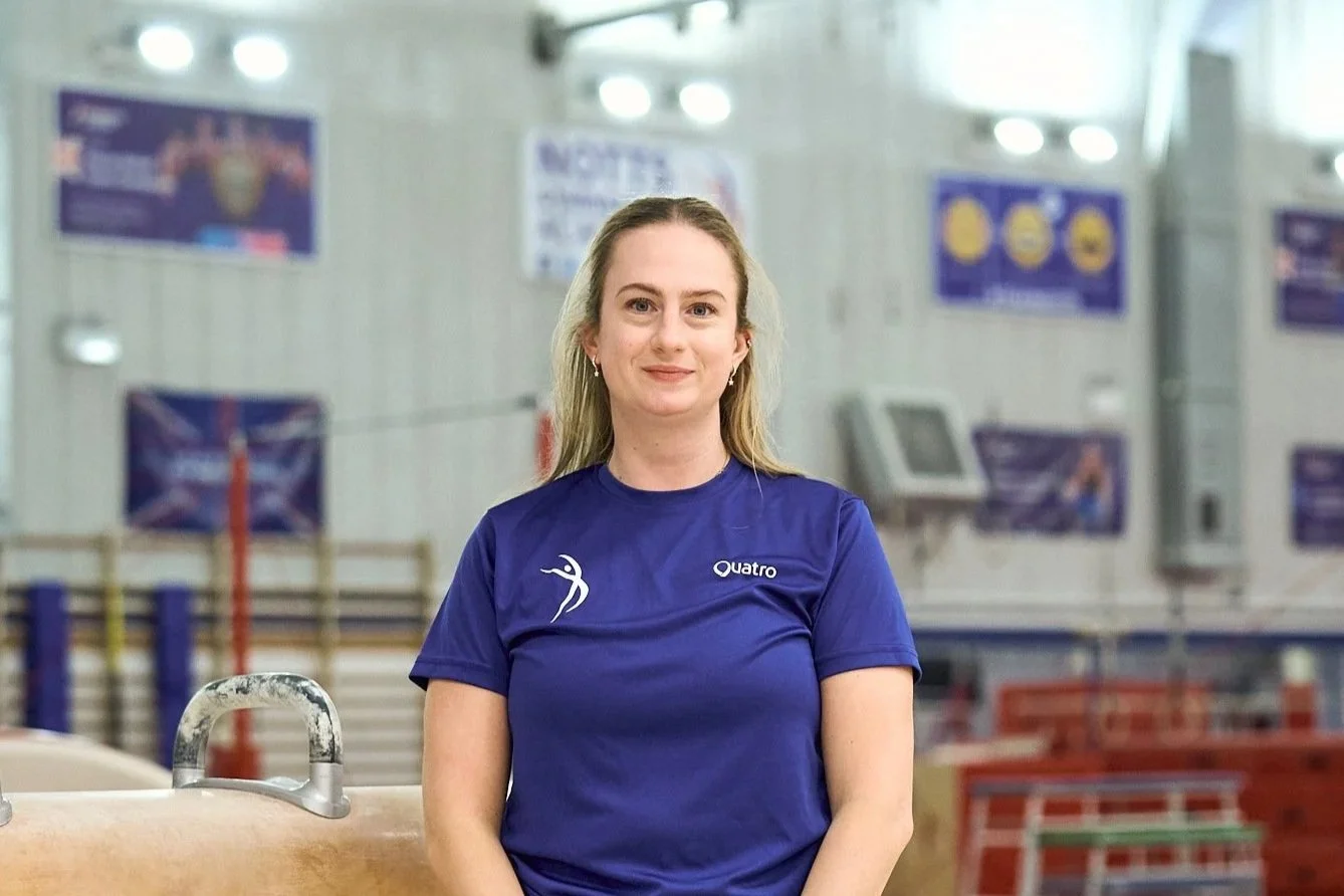 A young woman with blonde hair, blue eyes, and light skin, smiling slightly, wearing a blue shirt against a plain background.